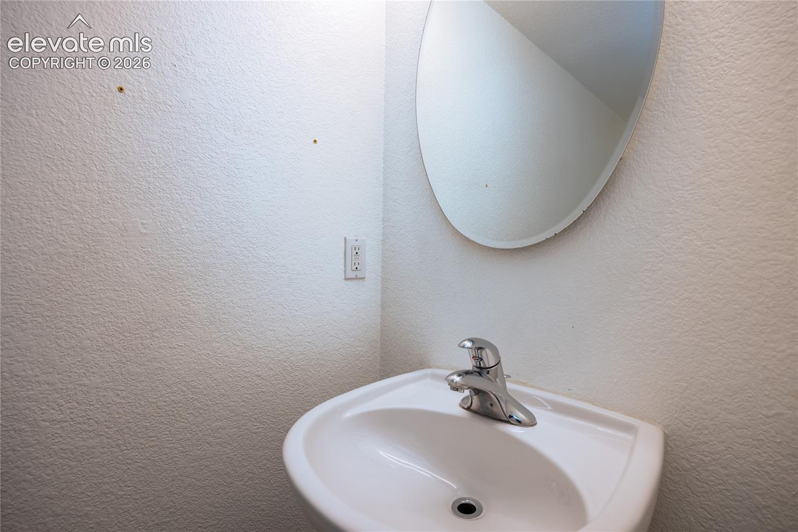 Pedestal sink with a chrome faucet and a wall-mounted oval mirror