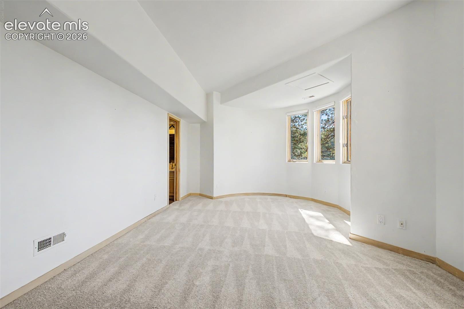 Curved architectural wall with three windows, neutral carpet flooring, and white walls
