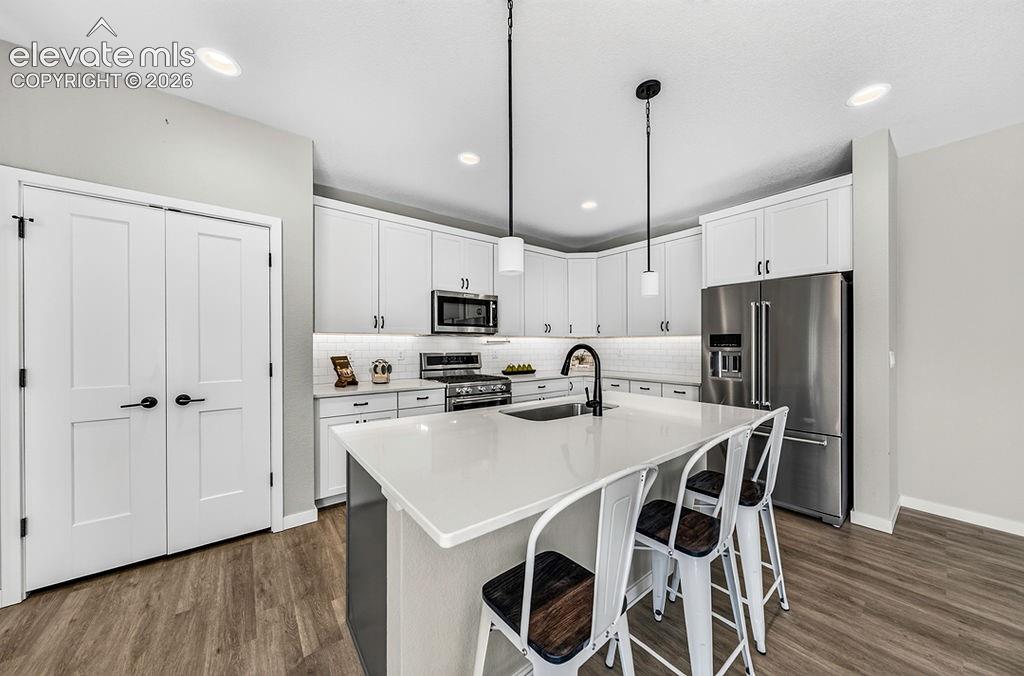 Modern kitchen featuring a central island with a solid surface countertop, white shaker cabinetry, stainless steel appliances, and wood-finish flooring