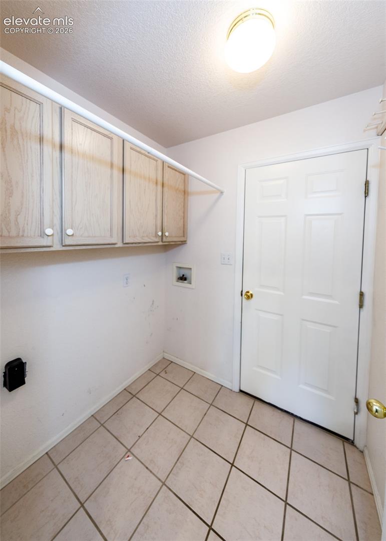 Utility space featuring ceramic tile flooring, wall-mounted light-toned wood cabinetry, and built-in white overhead storage rod
