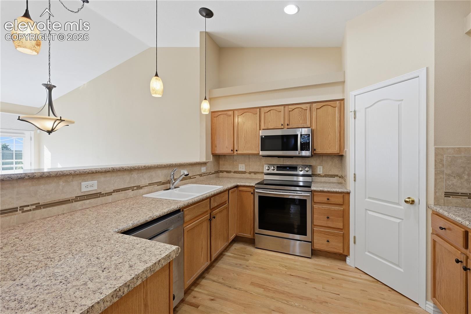 Kitchen featuring wood-finish cabinetry, stainless steel appliances, stone-surface countertops, tile backsplash, and pendant lighting