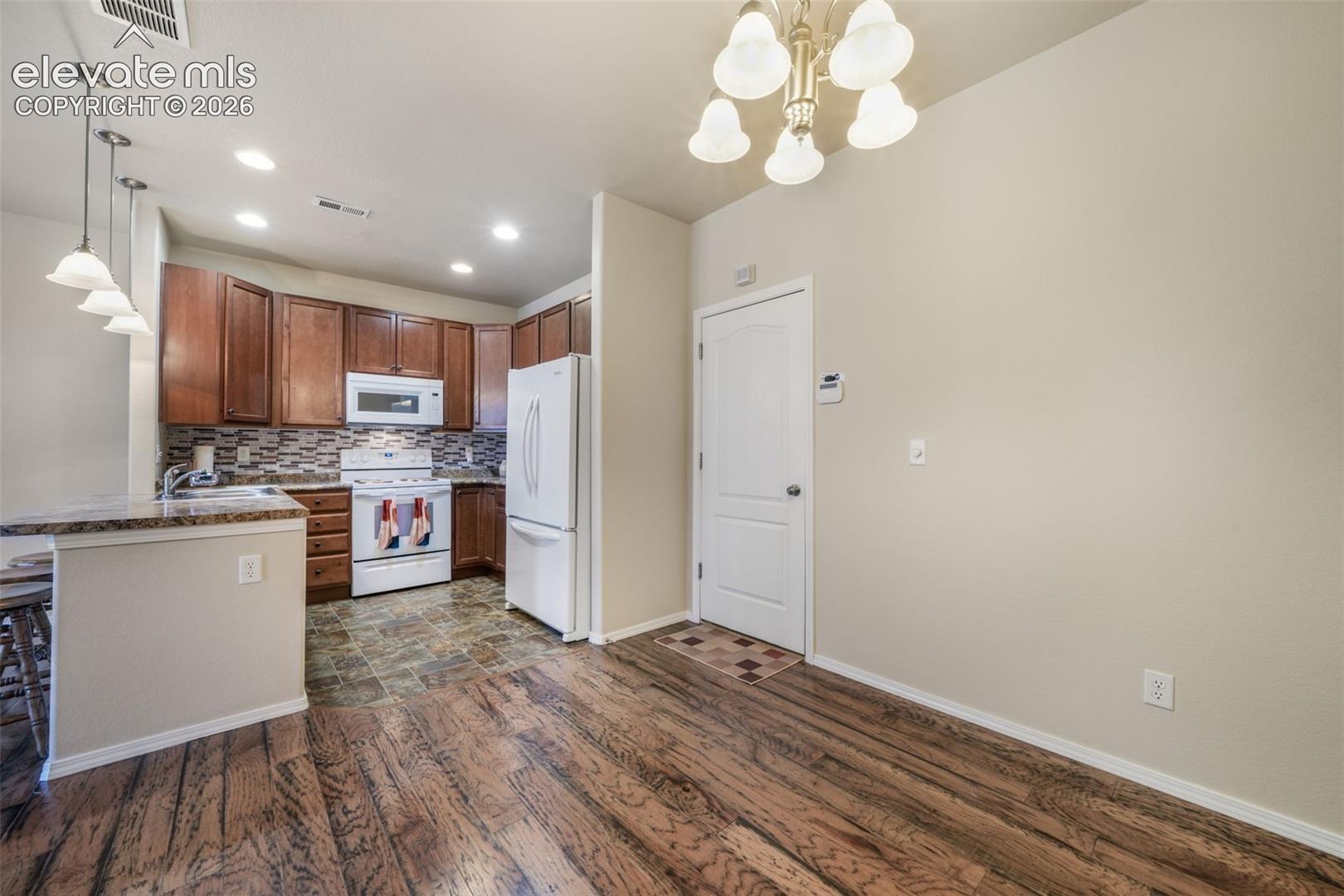 Kitchen featuring wood-finish cabinetry, white appliances, and a tiled backsplash