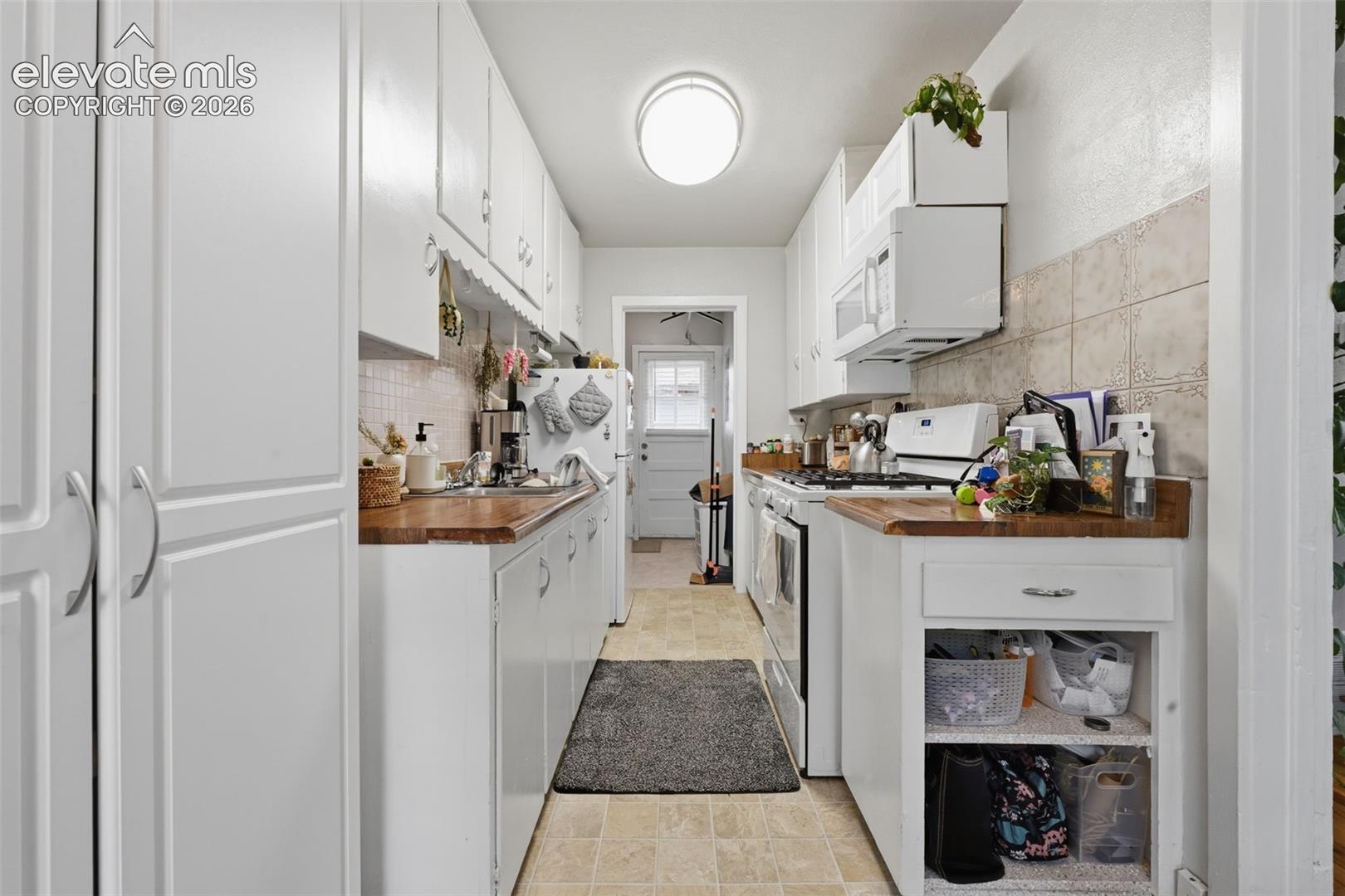 Galley kitchen featuring extensive white cabinetry, wood-finish countertops, and a tiled backsplash