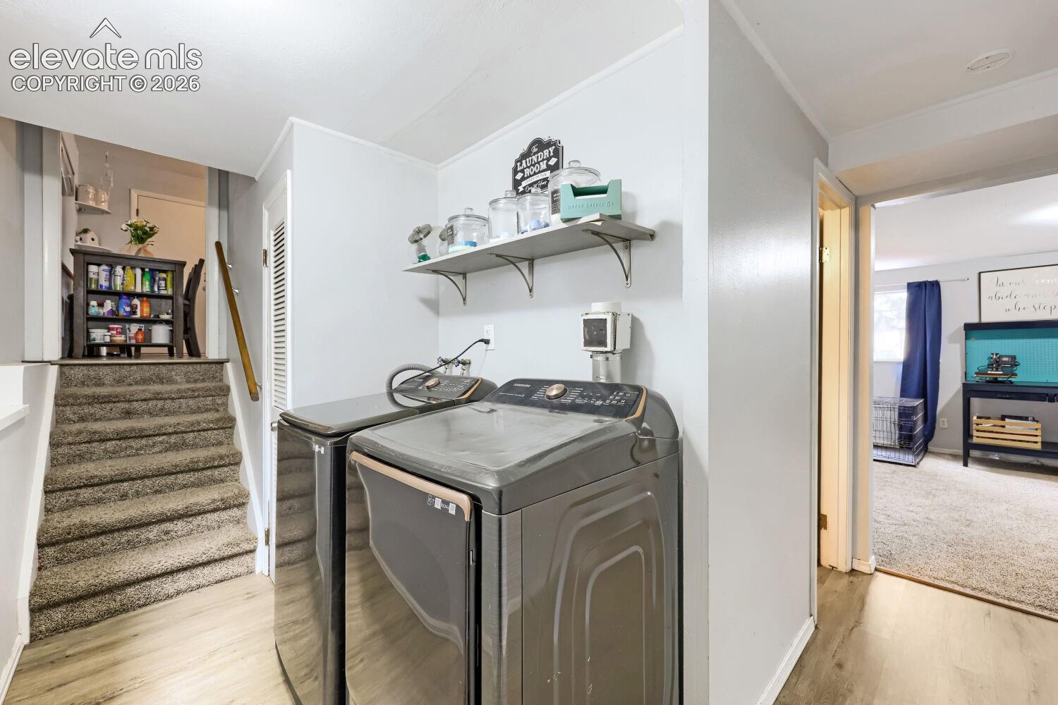 Laundry area featuring wood-finish flooring, two large-capacity appliances, and wall-mounted shelving