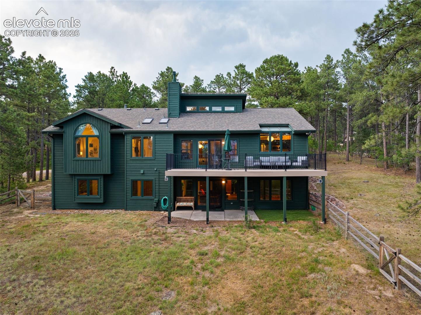 Multi-level residence featuring a deep green exterior, a second-story deck with a black metal railing, and a ground-level patio