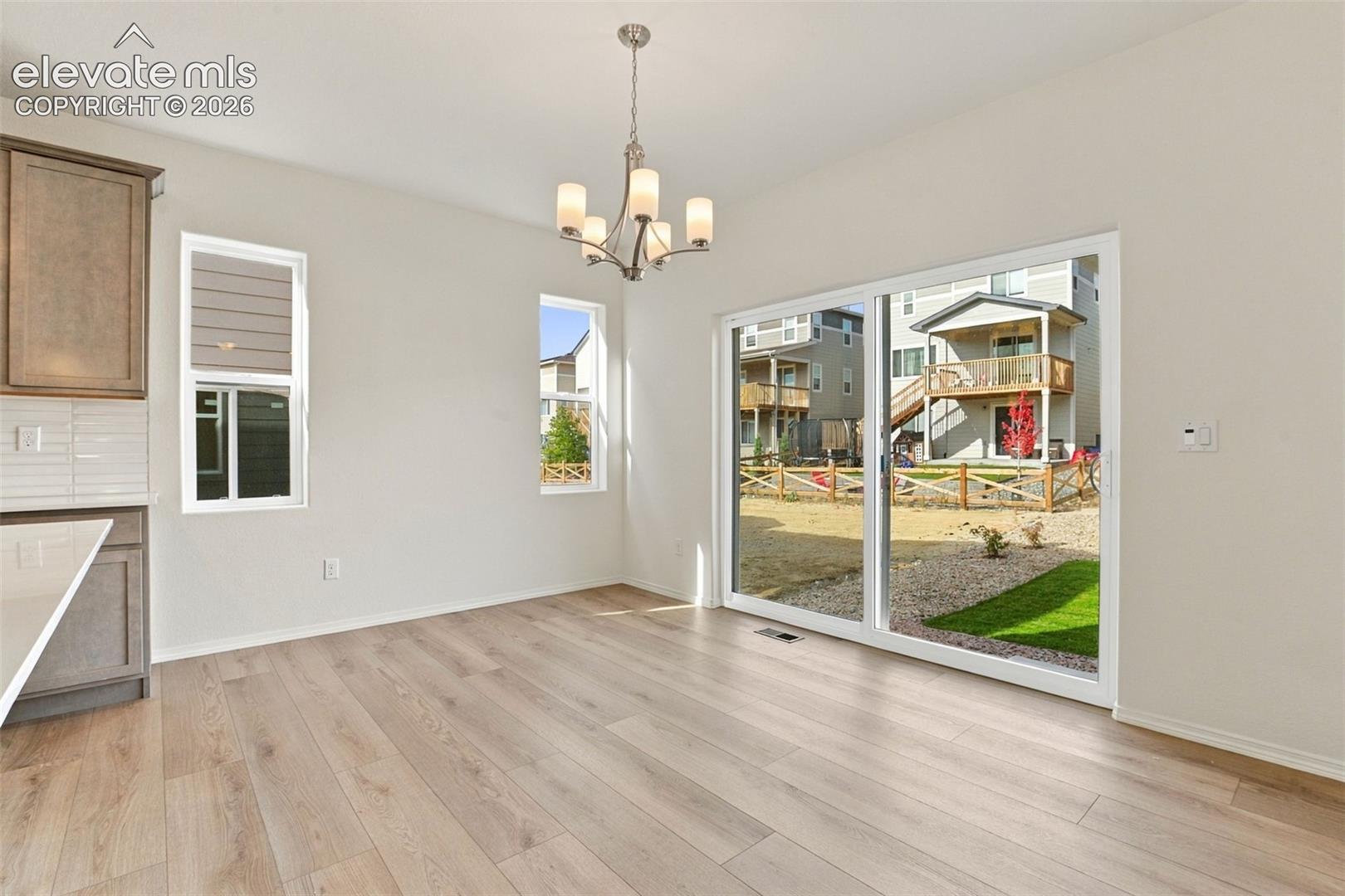 Dining area featuring wood-finish flooring, a contemporary multi-light chandelier, sliding glass patio doors, and cabinetry with tiled backsplash