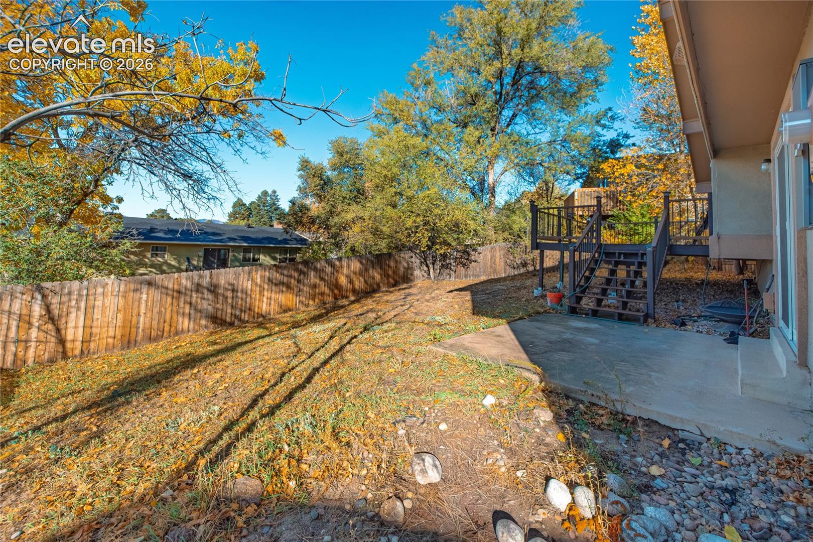 Backyard featuring a raised wooden deck with railings, concrete patio, wood privacy fencing, and mature trees