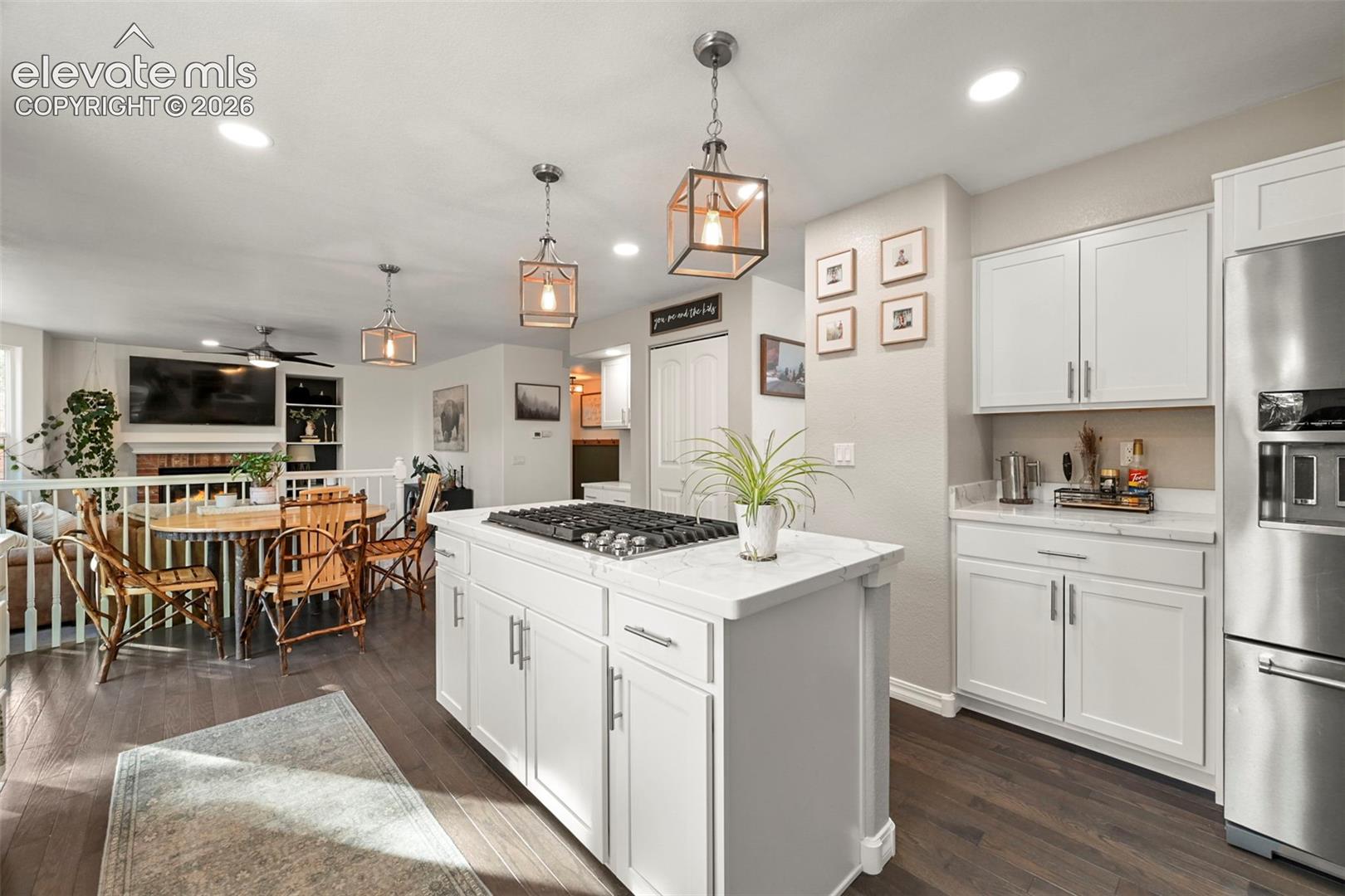 Kitchen featuring a central island with cooktop, white cabinetry, integrated stainless steel appliances, and wood-finish flooring