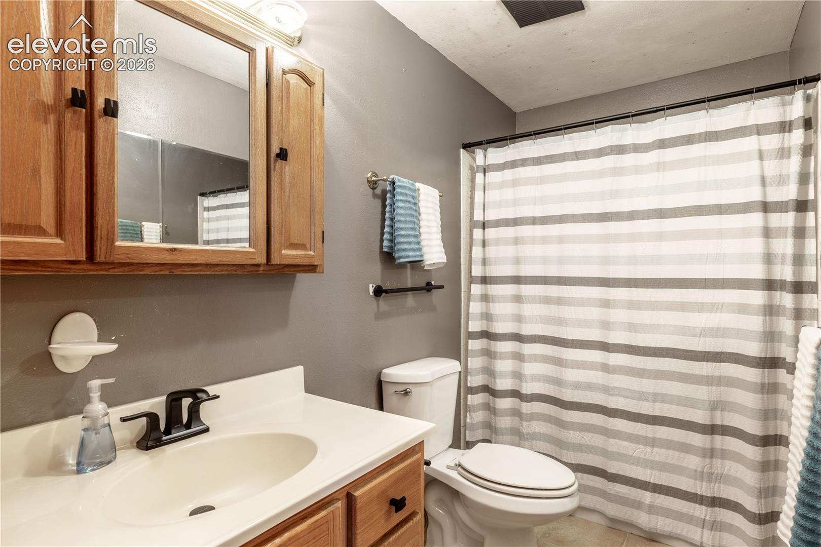 Bathroom featuring a vanity with wood-finish cabinetry, a white integrated sink, a matte black faucet, and a wall-mounted medicine cabinet with integrated lighting