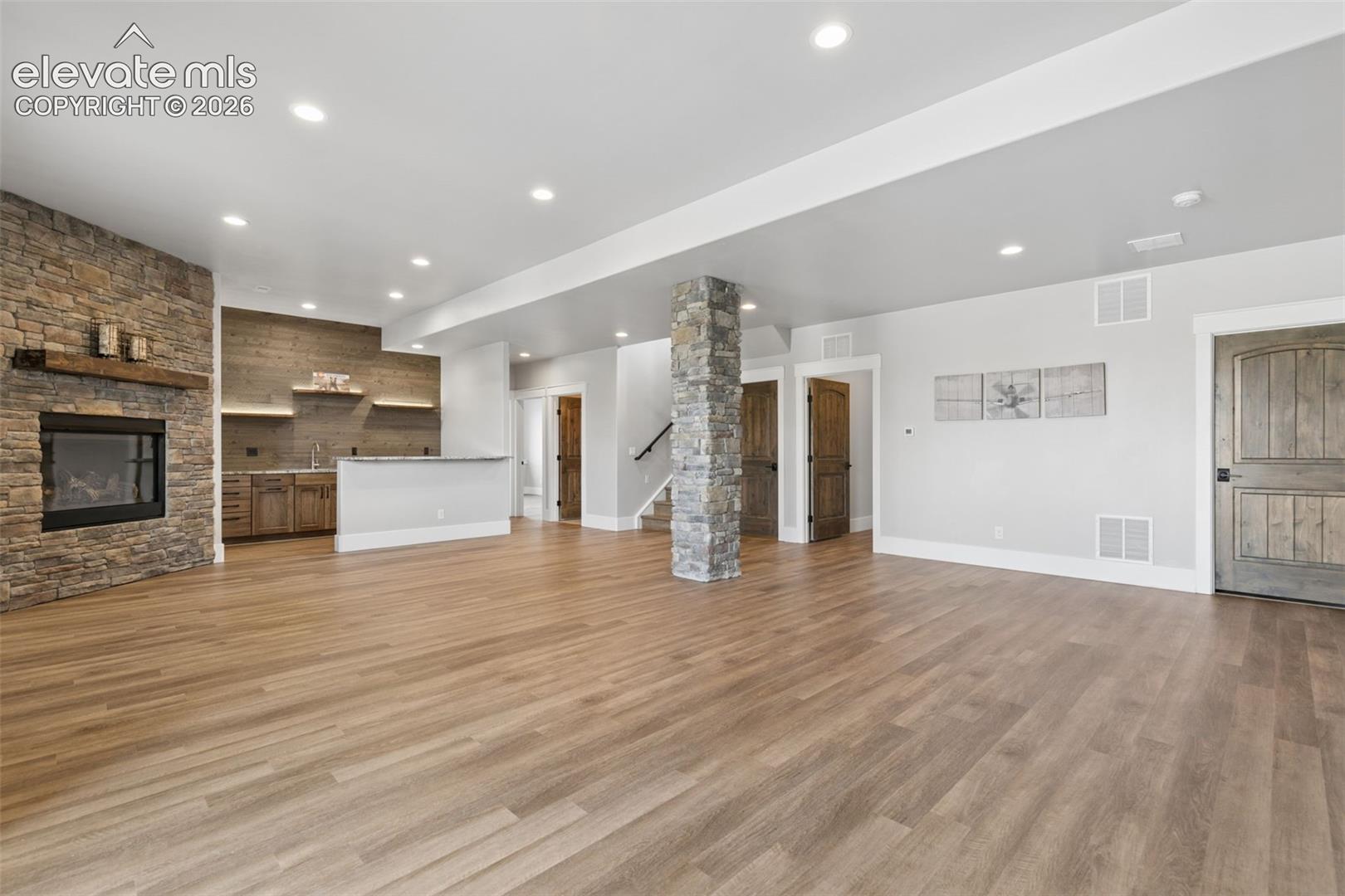 Spacious room featuring wood-finish flooring, a stone-clad fireplace, and a built-in wet bar with shelving