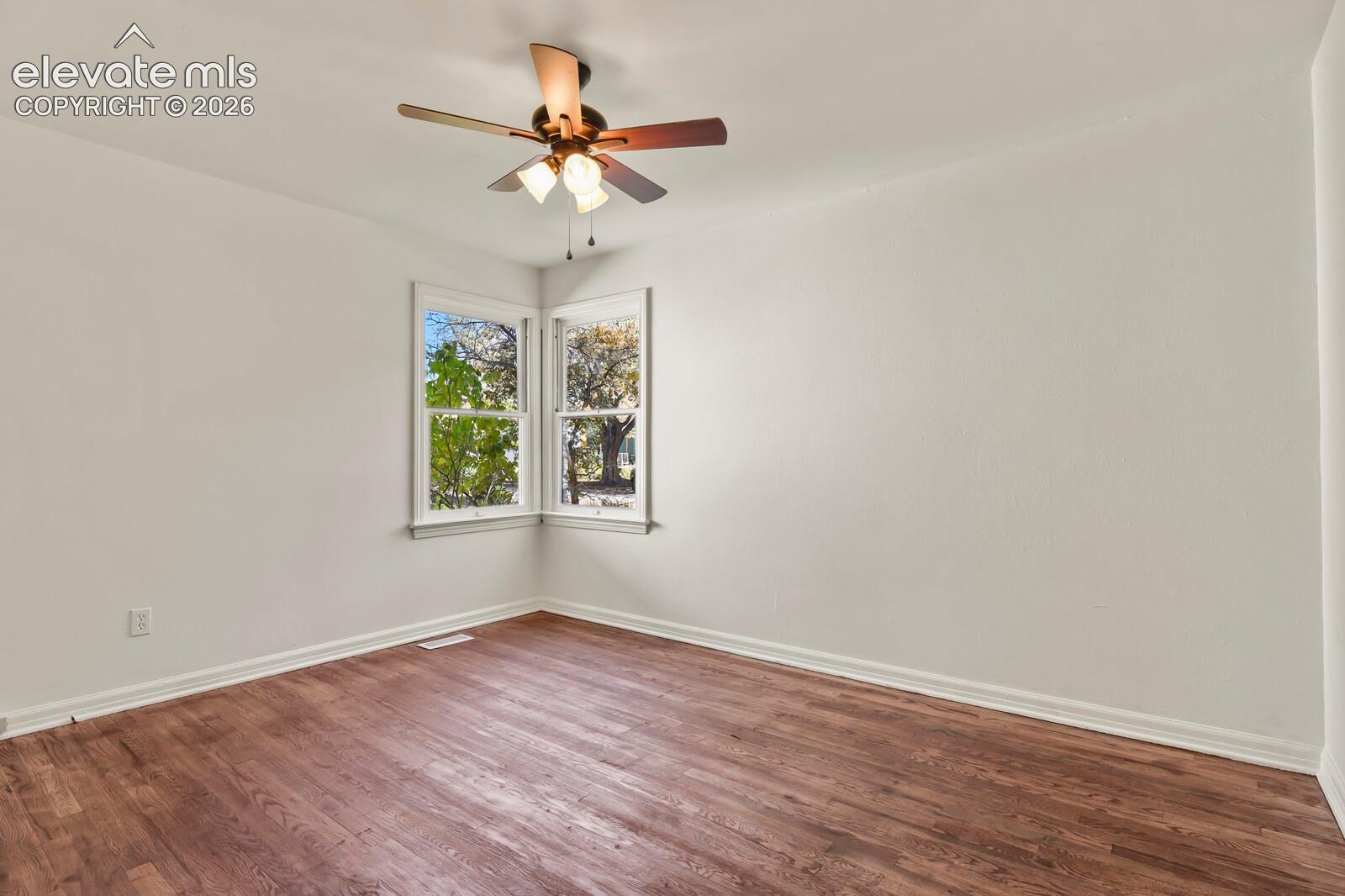 Room featuring wood-finish flooring, corner window configuration, and a multi-light ceiling fan