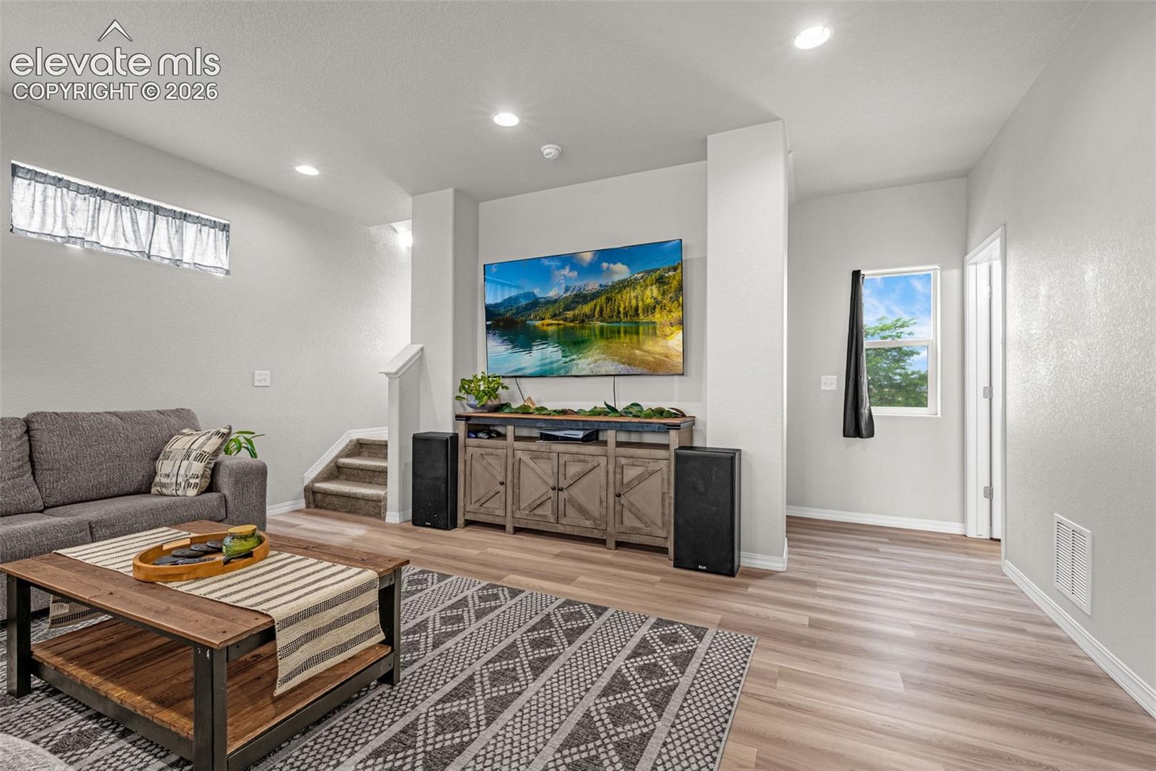 Spacious living area featuring light wood-finish flooring, recessed lighting, and a neutral color palette