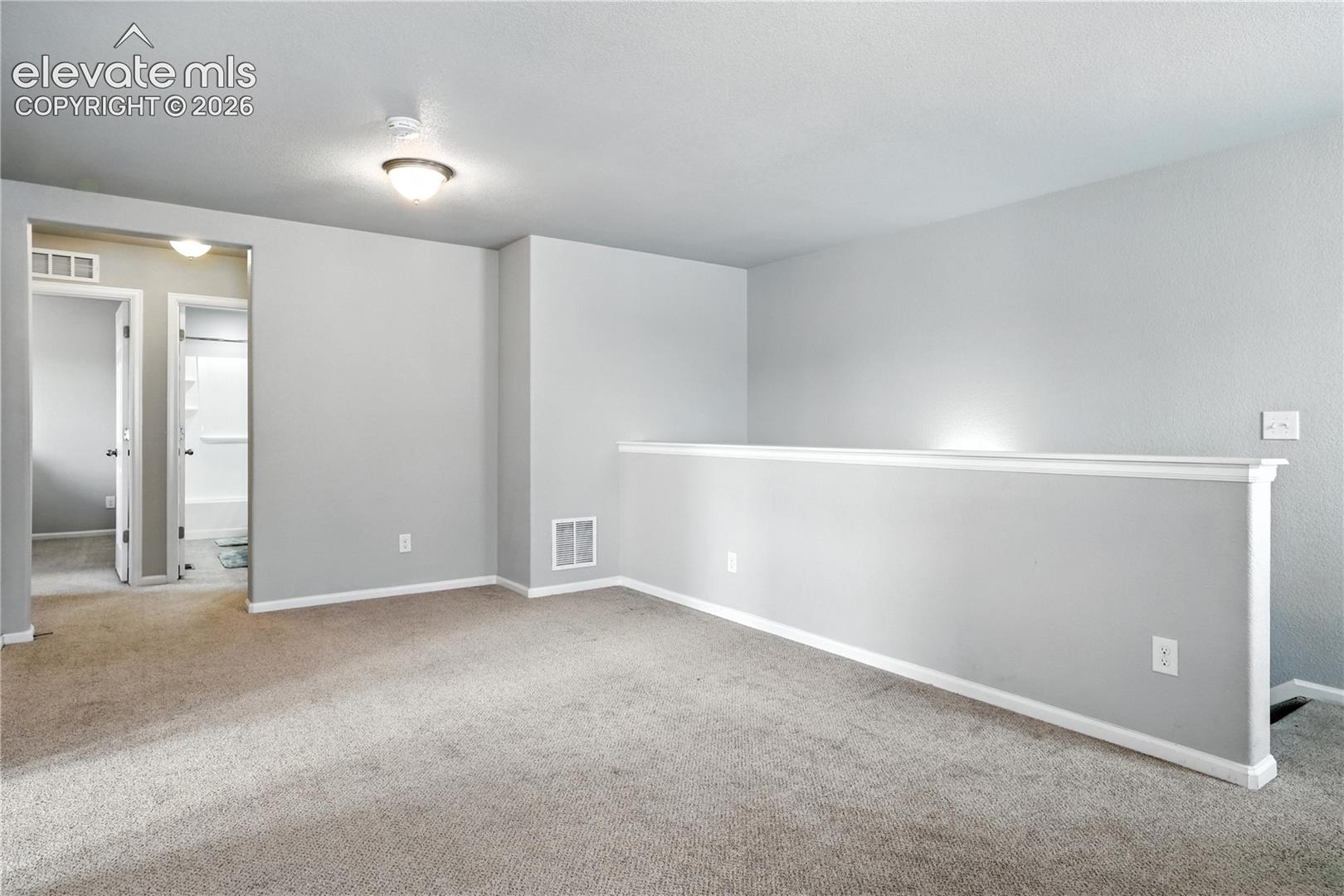 Carpeted loft area with light gray walls, white trim, and a flush mount ceiling light fixture