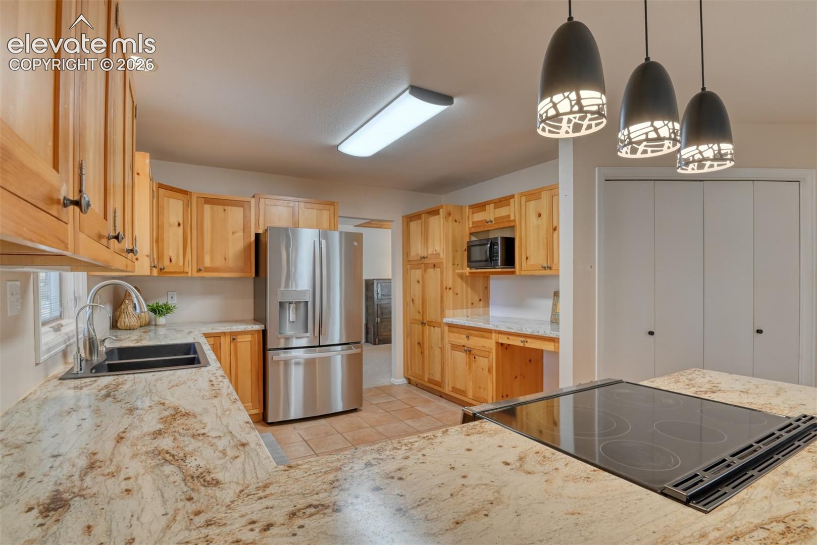 Remodeled kitchen featuring natural wood cabinetry, stainless steel refrigerator, built-in cooktop/range, and decorative pendant lighting