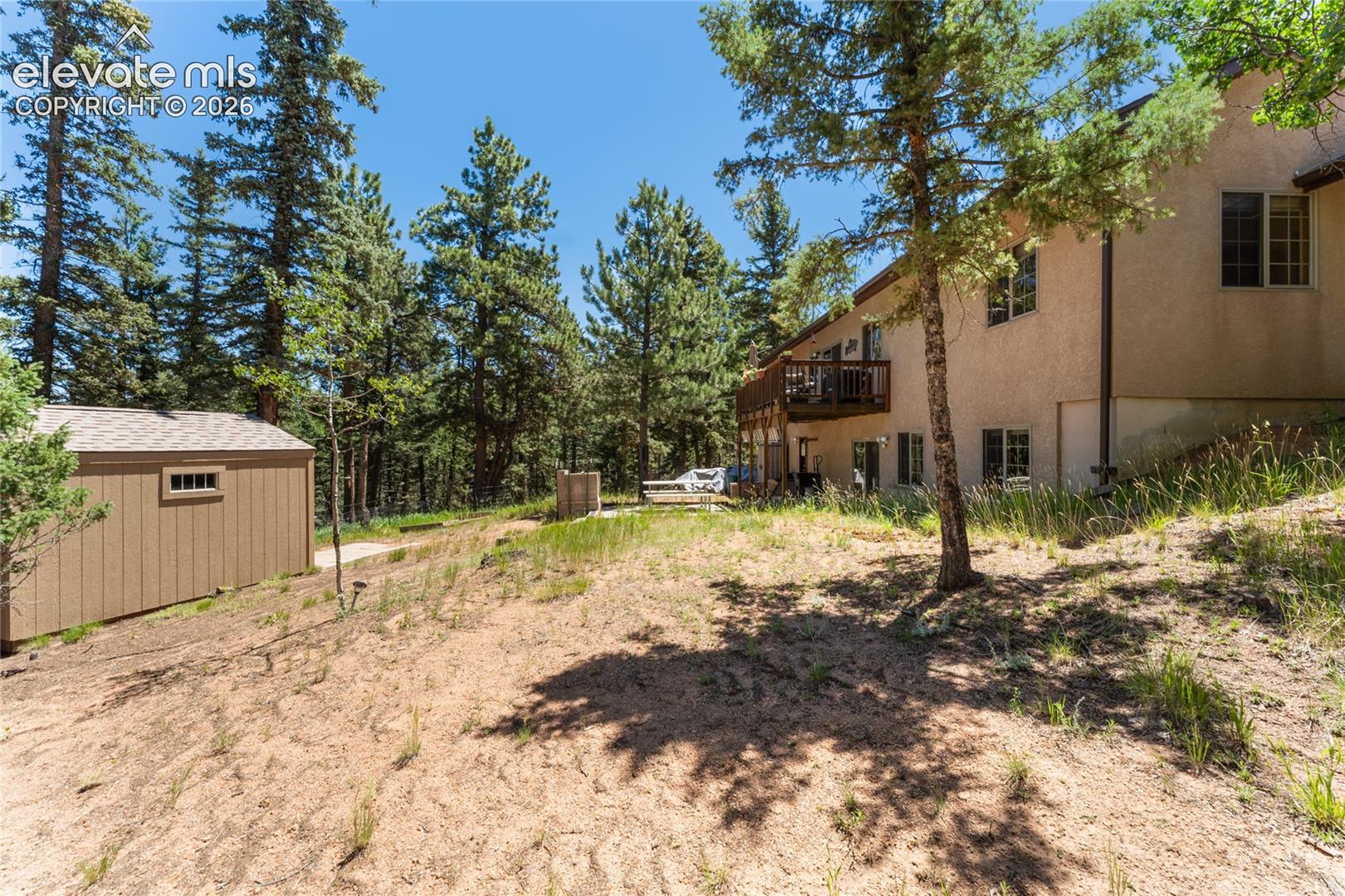 Stucco exterior dwelling with a tiered wooden deck, surrounded by mature pine trees