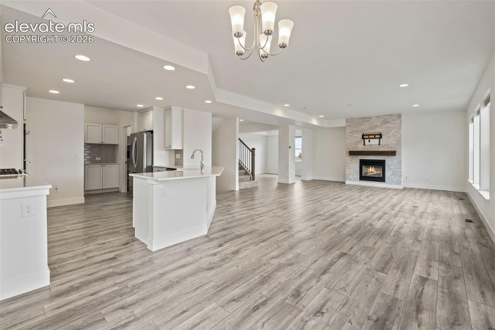 Expansive open-concept living area featuring wood-finish LVP flooring, a contemporary fireplace with a stone surround, recessed lighting, and a kitchen island with a farmhouse sink
