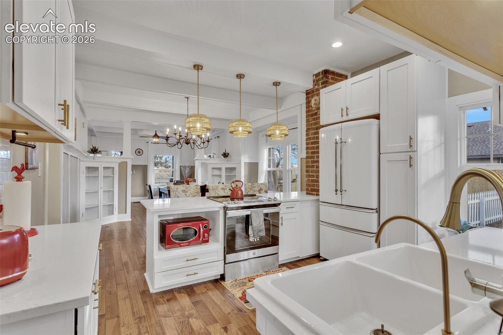 Spacious kitchen featuring white cabinetry, light countertops, wood-finish flooring, a double basin sink with a brass faucet, and white appliances