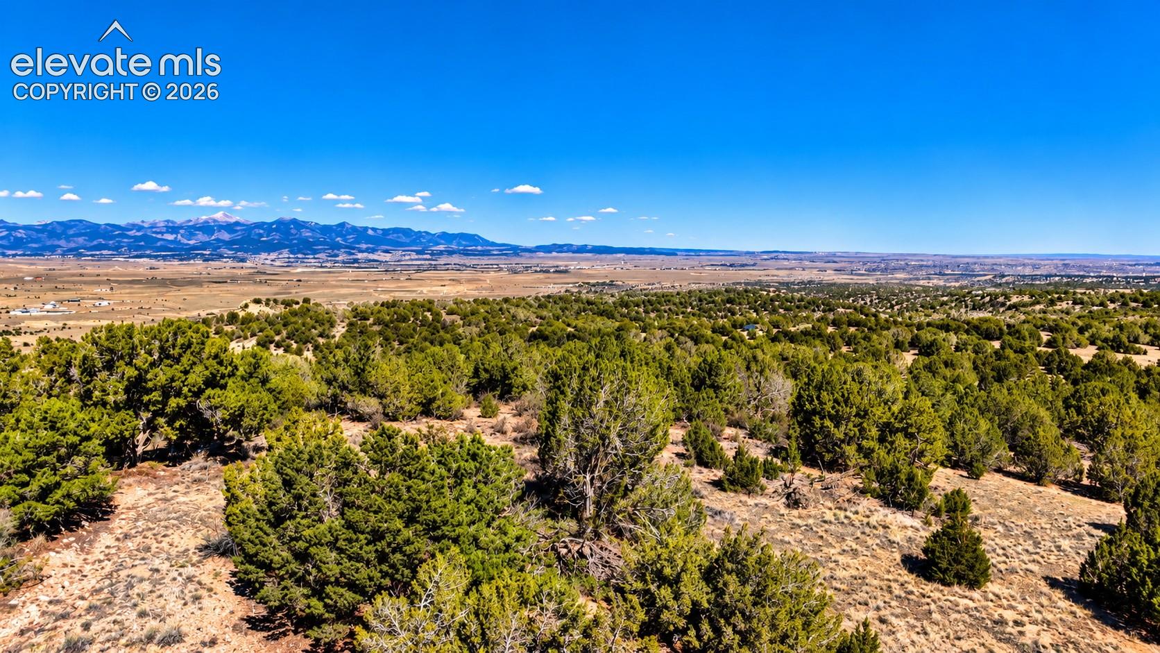 LandscapeExpansive aerial view of rugged ridgelines, natural ravines, and rolling hills covered in native vegetation, with mountain ranges stretching across the horizon.

