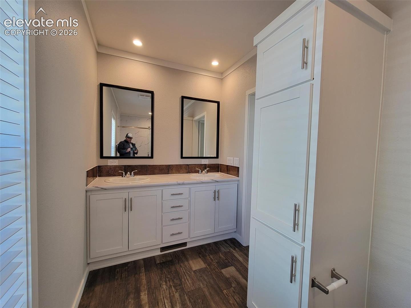 Double vanity featuring white cabinetry, a countertop with dual drop-in sinks, a tall storage pantry, and wood-finish flooring