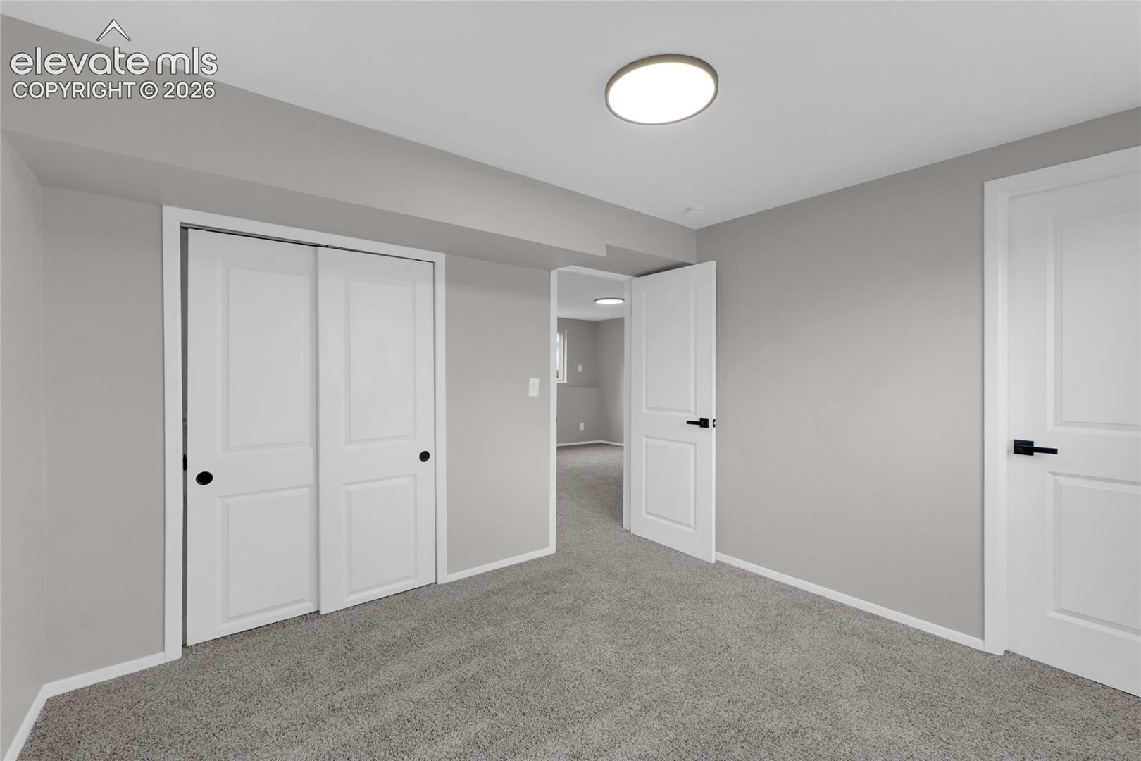 Wall-to-wall carpeting with light gray walls, featuring white trim and white interior doors with black hardware