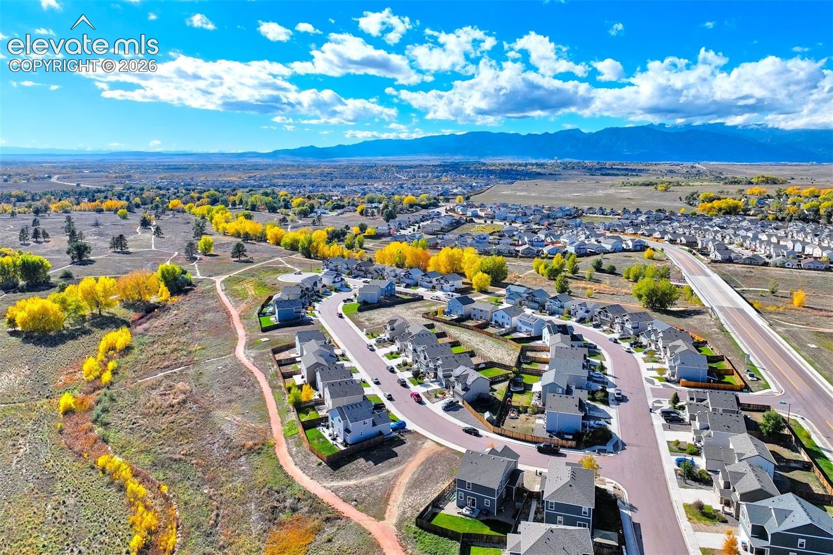 Aerial perspective featuring residential lots with mountain backdrops, paved roads, and perimeter natural landscaping