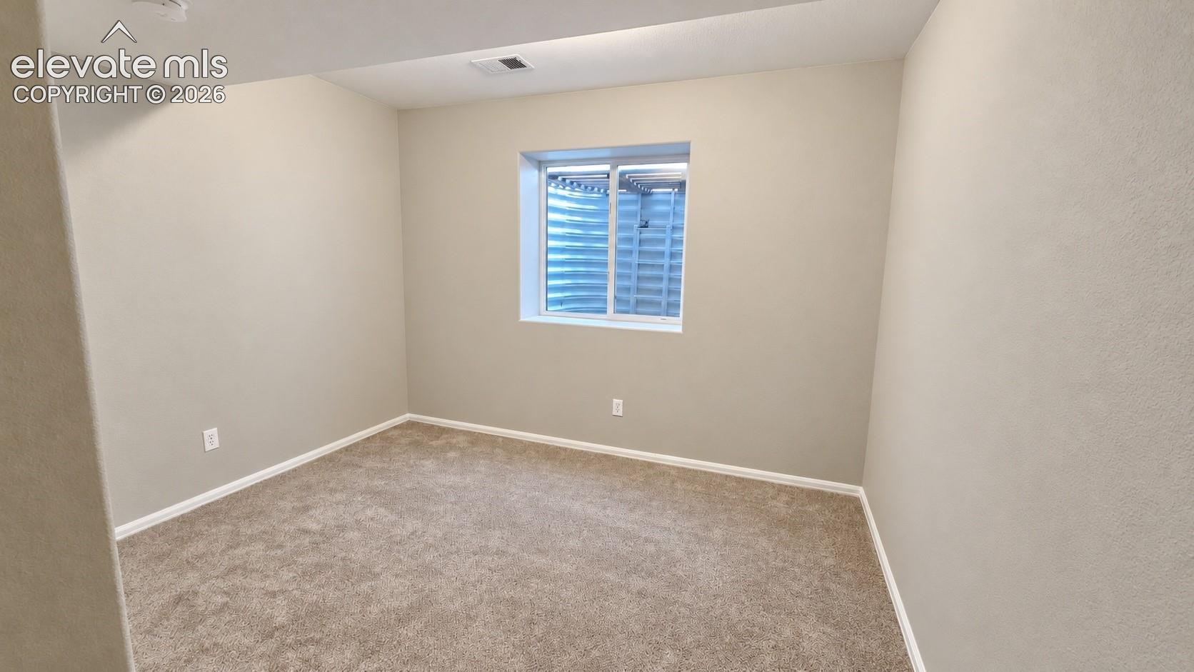 Neutral-toned interior space featuring carpeting, smooth wall finishes, and a single-pane sliding window with an external corrugated metal window well