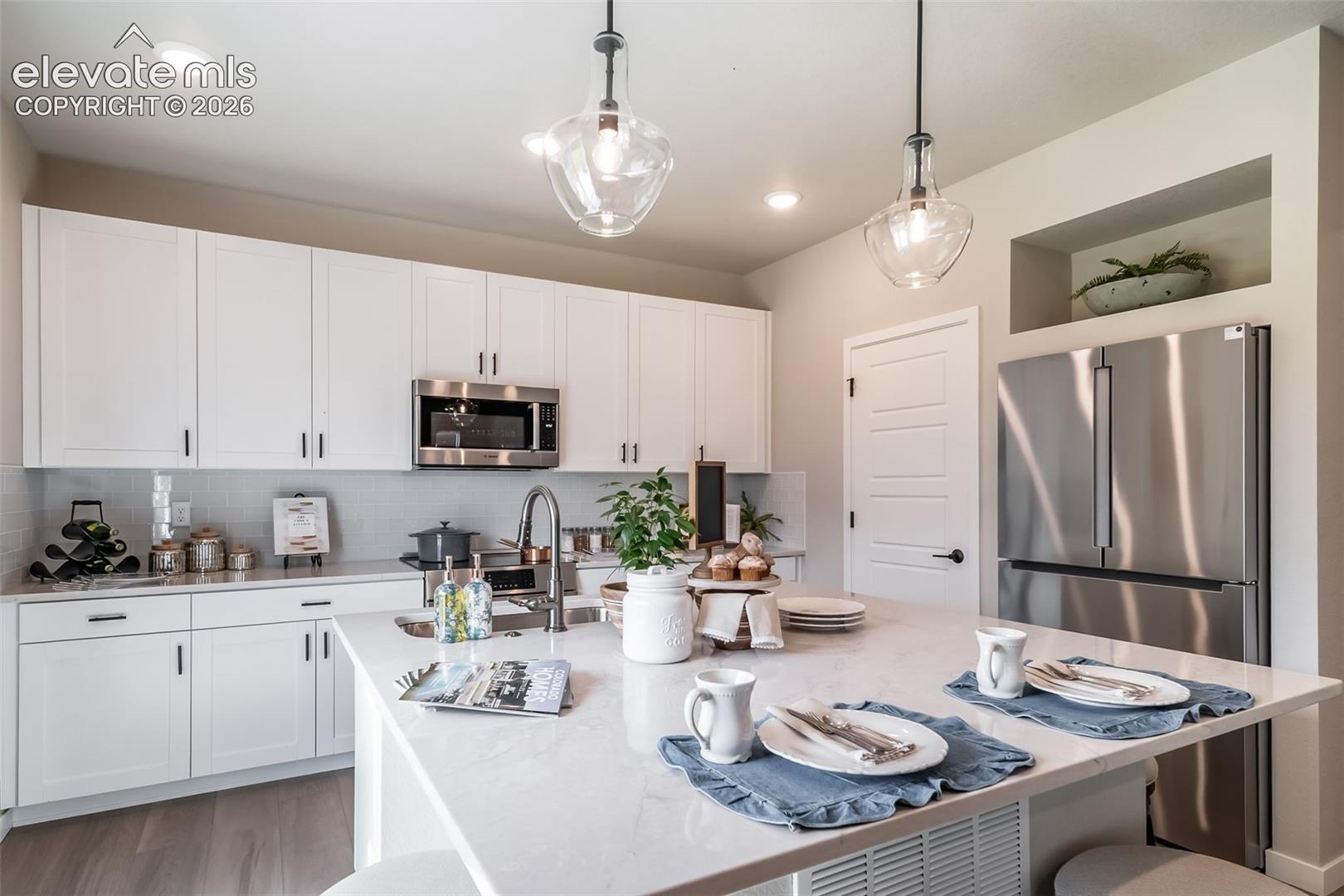 Gourmet kitchen featuring a large island with seating, stainless steel appliances, white shaker cabinetry, recessed lighting, and a subway tile backsplash
*Photos of a model home*