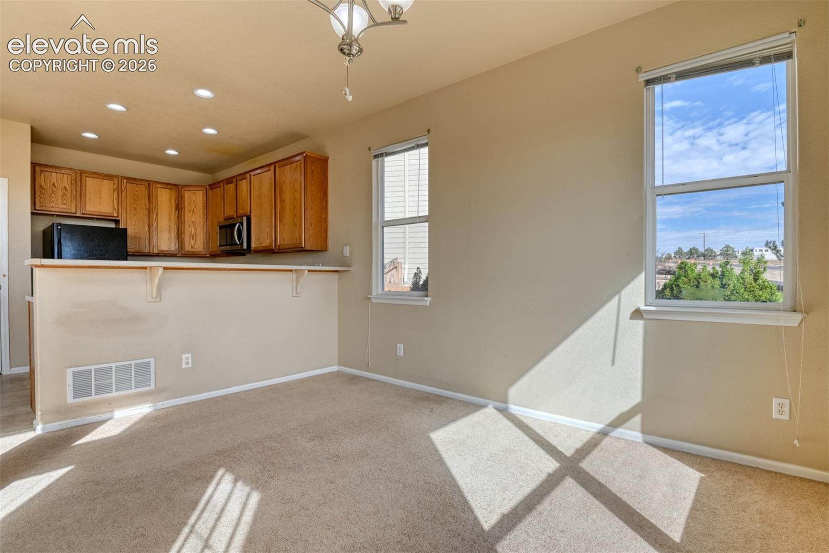 Open-concept area featuring a breakfast bar with wood cabinetry, dual pane windows, recessed lighting, and a multi-arm ceiling fixture