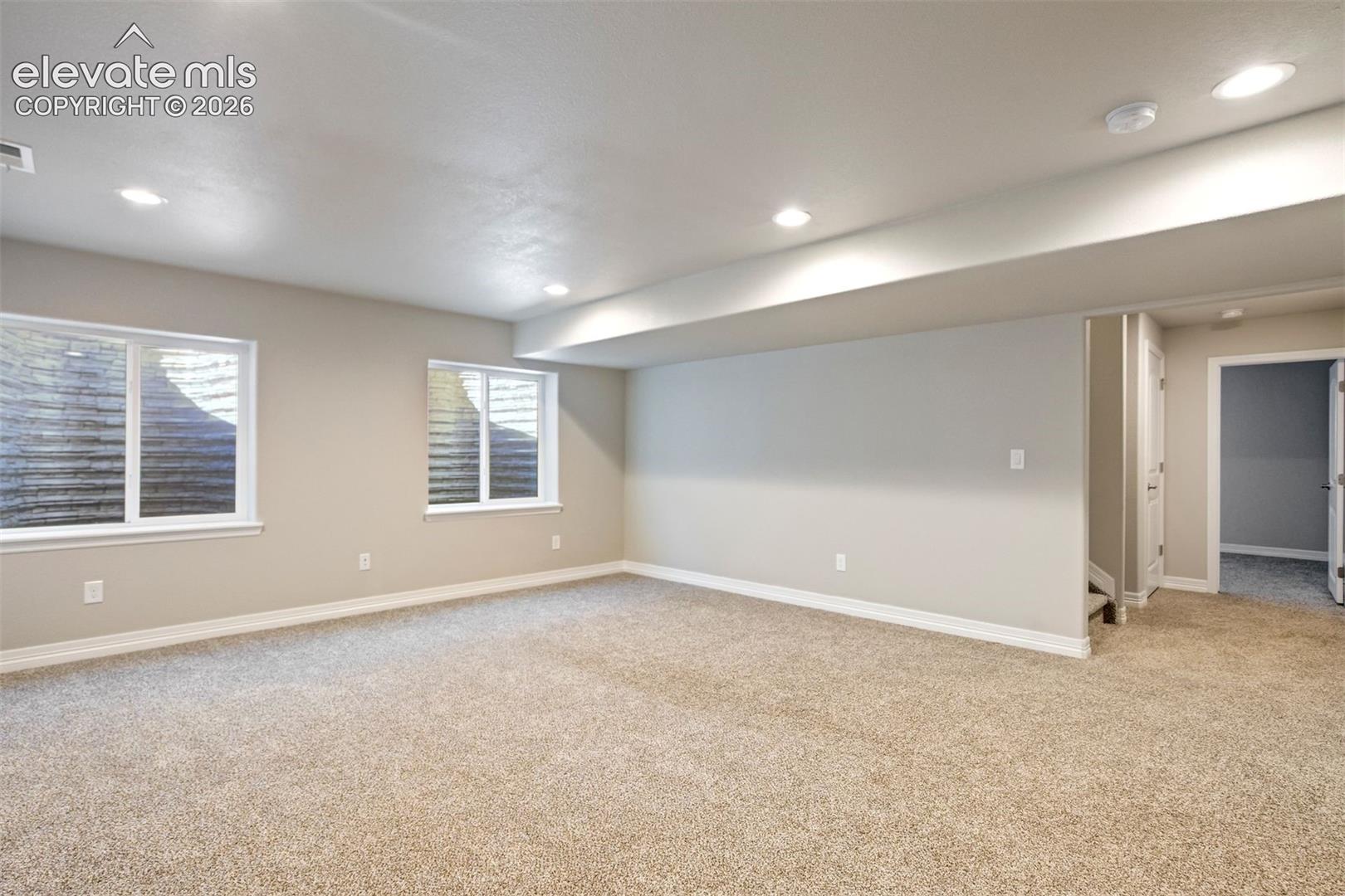 Recessed lighting, light-colored carpeting, two egress windows, neutral wall tones, and white trim