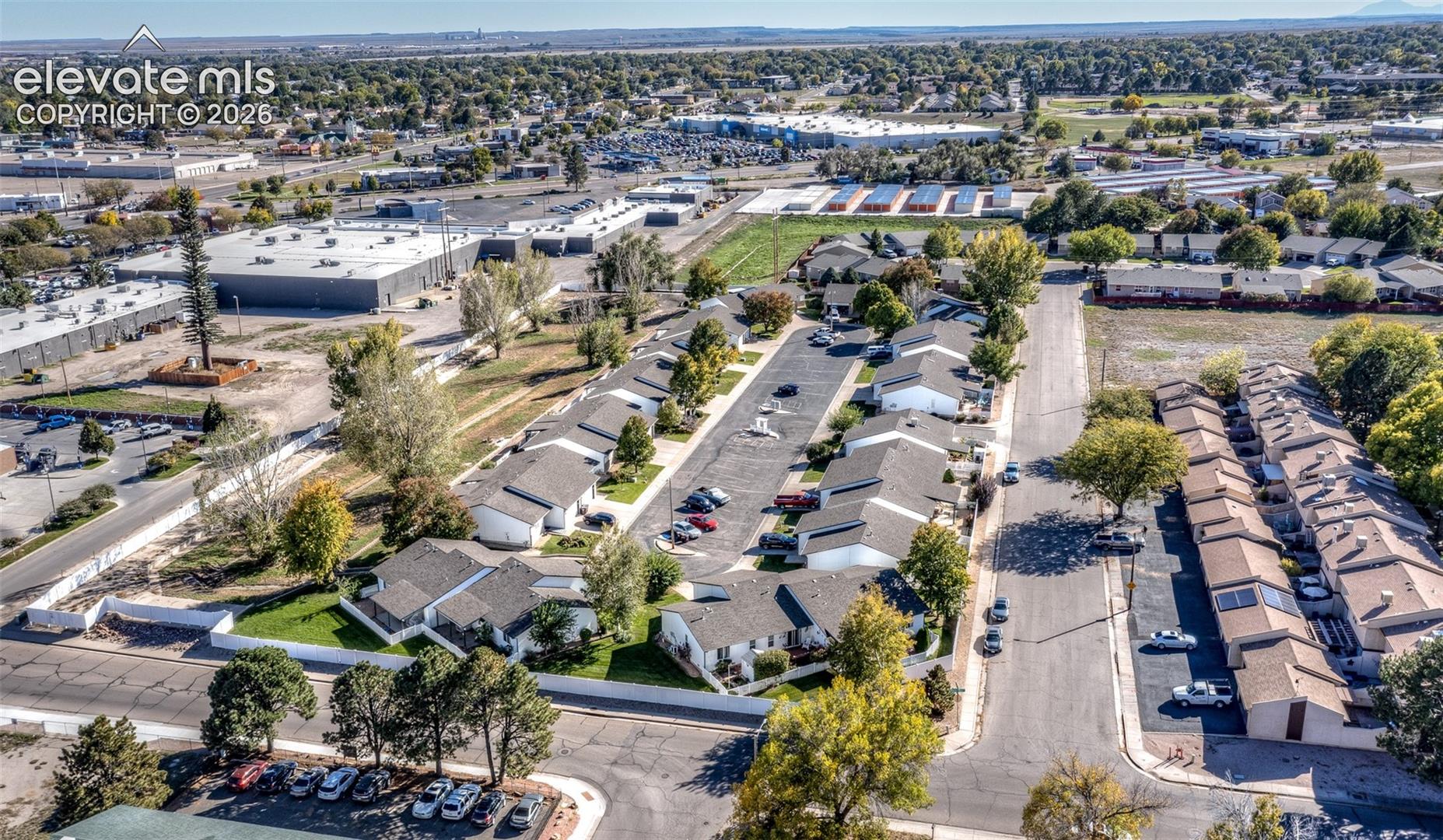 Aerial perspective featuring a residential community with paved access roads, established mature trees, and designated surface parking