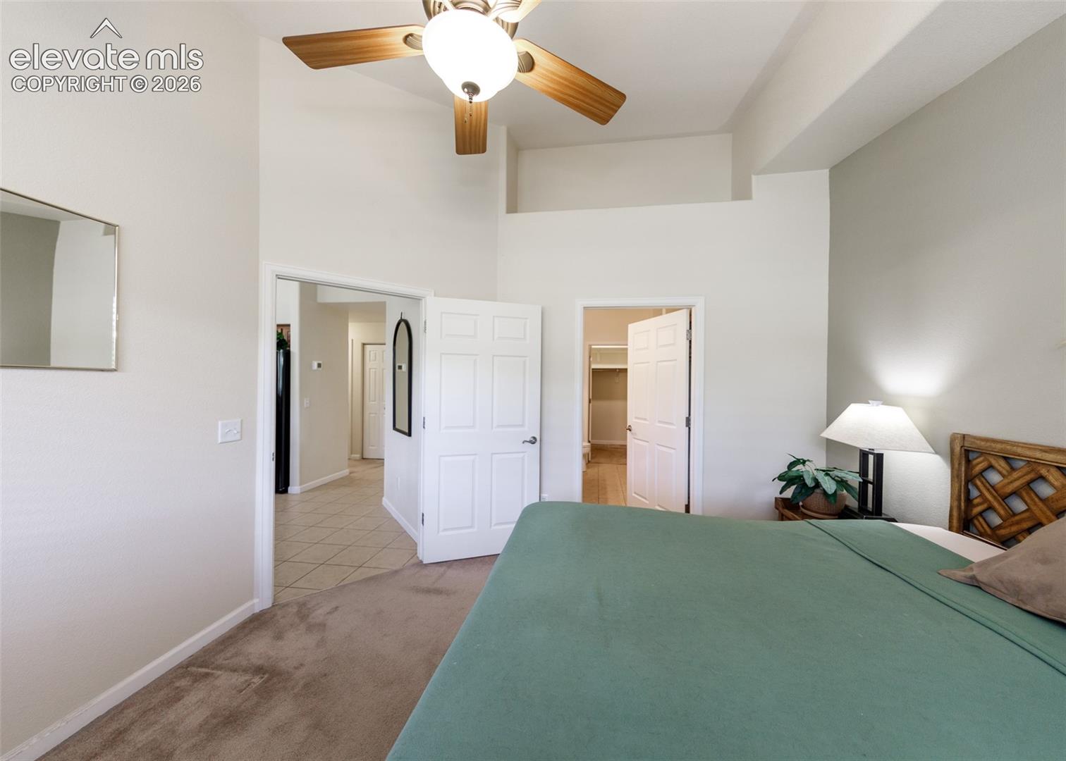 Vaulted ceilings featuring an integrated ceiling fan with light fixture, neutral carpeted flooring, and six-panel interior doors