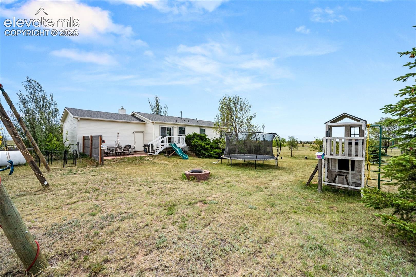 Expansive rear yard featuring a paved patio, multi-level deck with white railing, and a fire pit
