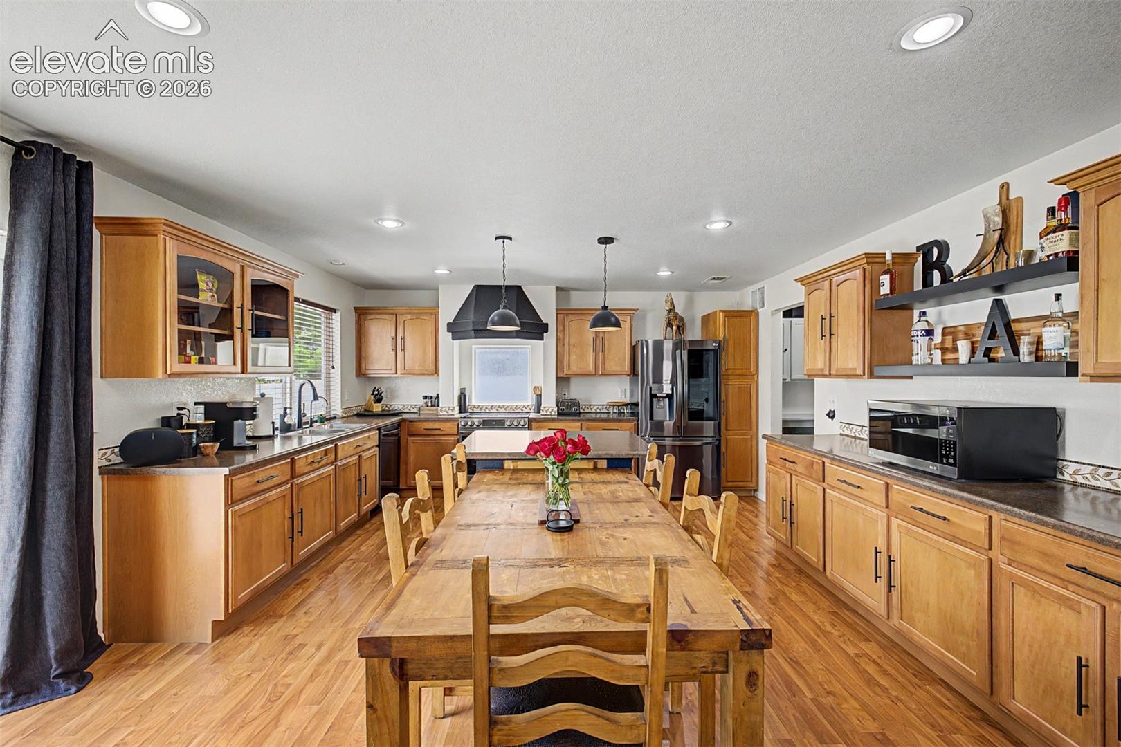 A chef's kitchen with warm maple cabinetry, dark countertops, a striking matte-black range hood, and a dramatic farmhouse dining table make this space the undeniable heart of the home.
