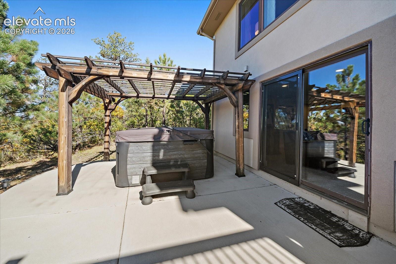 Concrete patio featuring a wood pergola and an integrated hot tub, complemented by a sliding glass door exterior entry