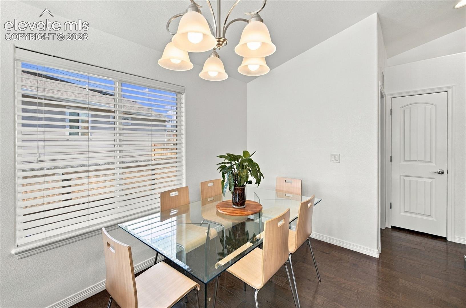 Wood-finish flooring, five-light brushed nickel chandelier, horizontal slat blinds, and a two-panel arched interior door