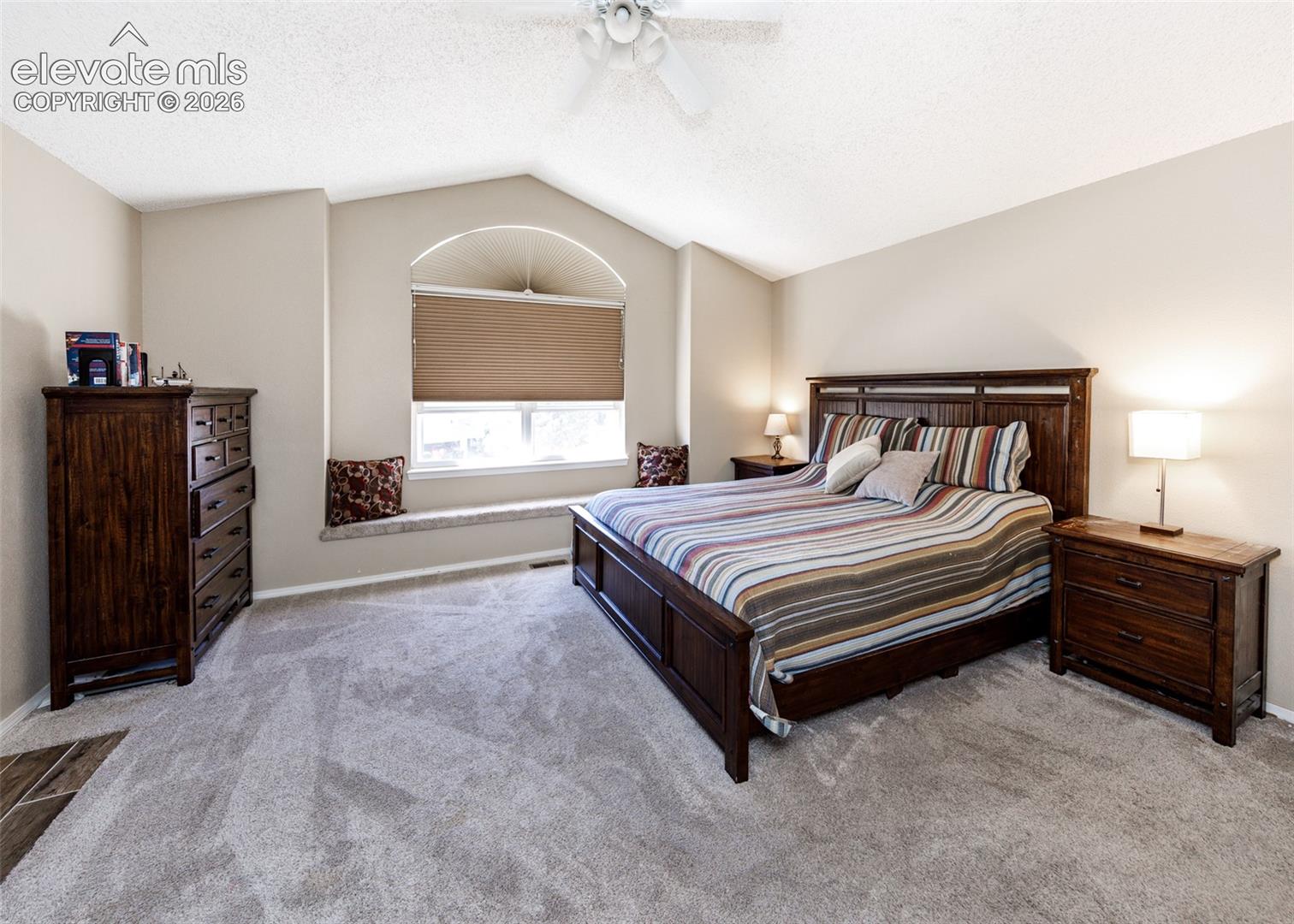 Vaulted ceiling with a ceiling fan, arched window with a window seat, and carpet flooring