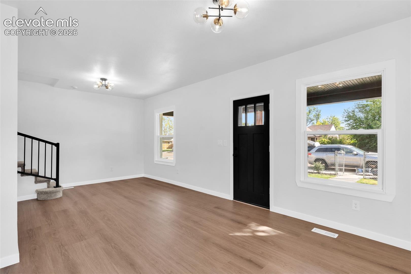 Interior space featuring wood-finish flooring, modern multi-globe chandelier lighting, a black front door with glass inlay, and a staircase with black metal balusters