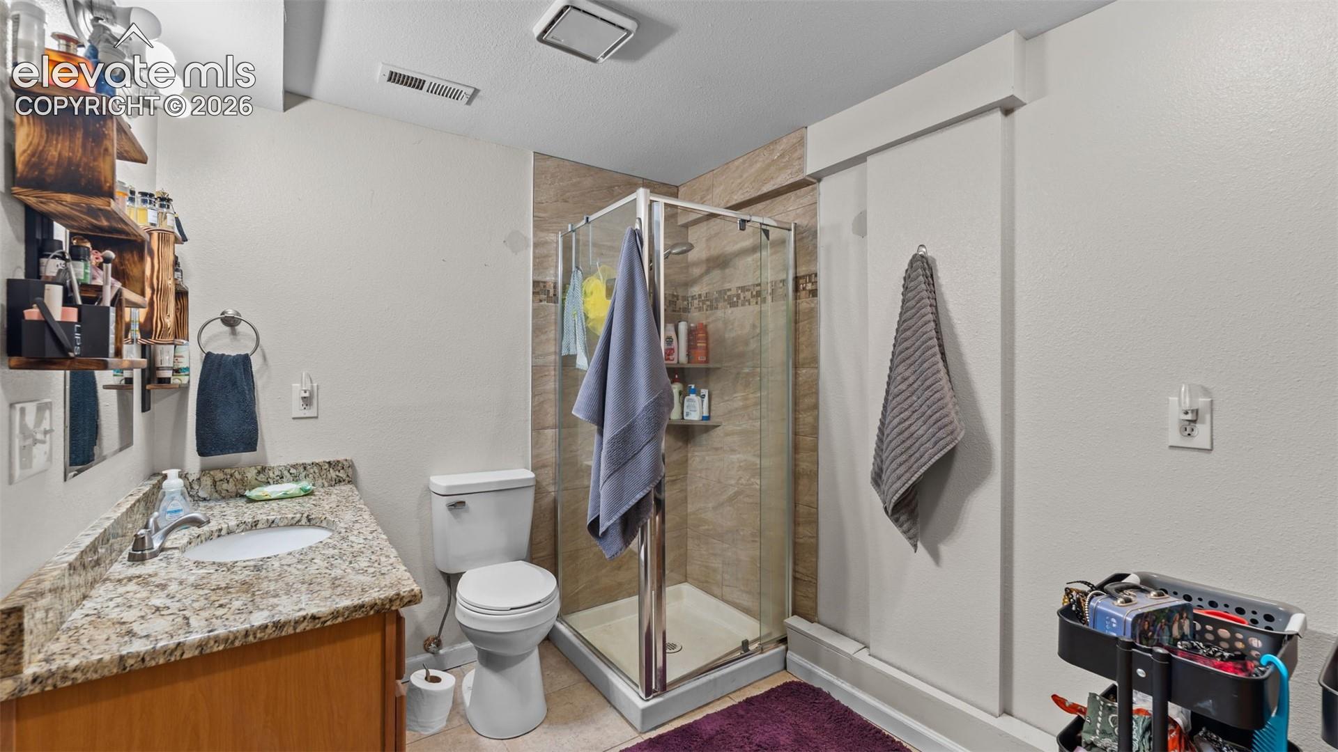 Bathroom featuring a vanity with stone-patterned countertop, under-mount sink, chrome faucet, and a glass-enclosed shower with tiled surround