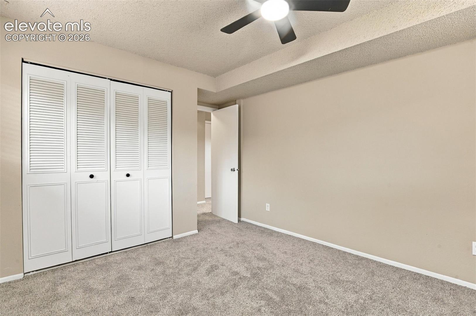 Room featuring wall-to-wall carpeting, white bi-fold louvered closet doors, and a ceiling fan with integrated lighting