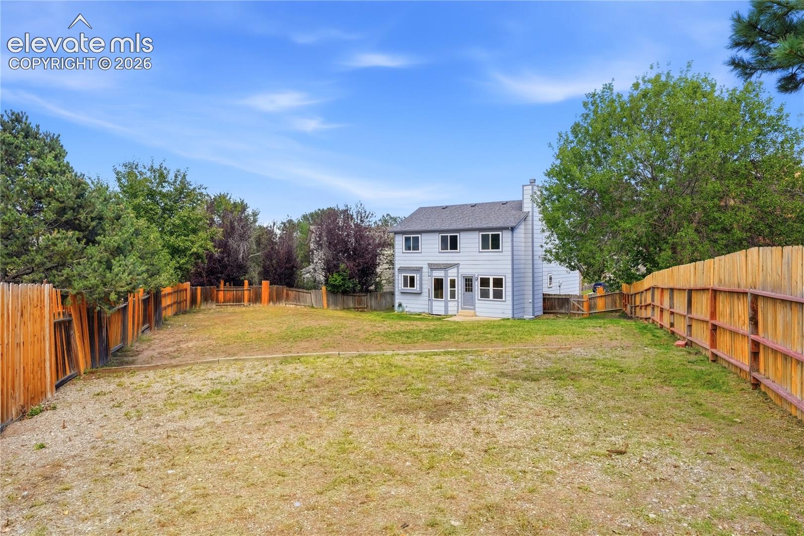 Expansive backyard with a full perimeter wood fence, and a light-colored two-story exterior