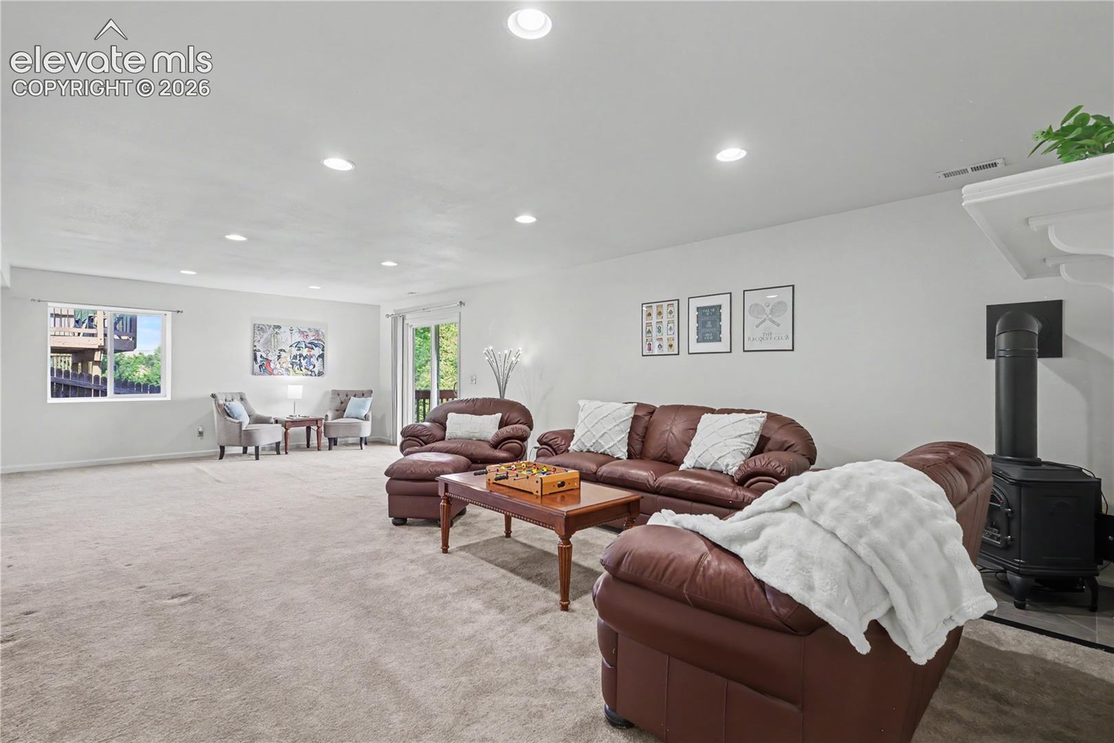 Spacious carpeted room featuring recessed lighting, a built-in wood-burning stove, and a glass sliding door providing outdoor access
