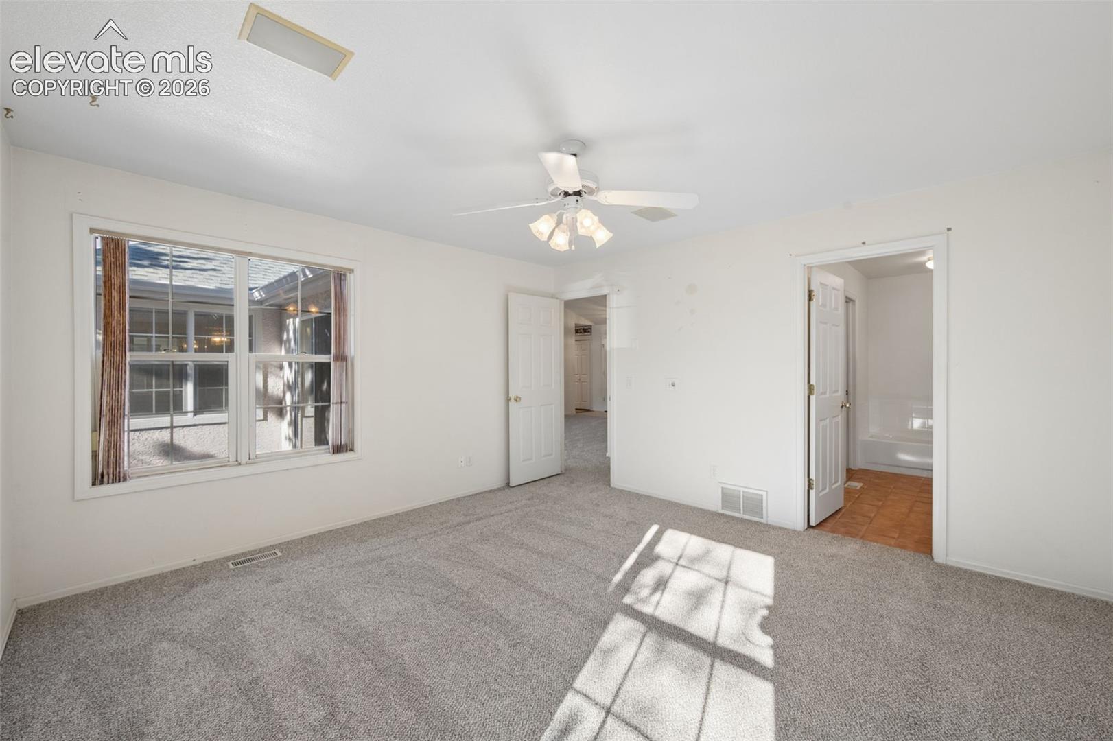 Room featuring neutral carpeting, a central ceiling fan with integrated lighting, and a multi-pane window