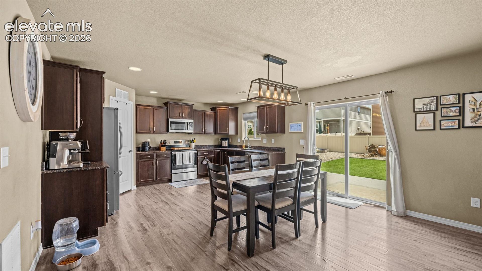 Open-concept kitchen and dining area featuring rich wood cabinetry, stainless steel appliances, and wood-finish flooring