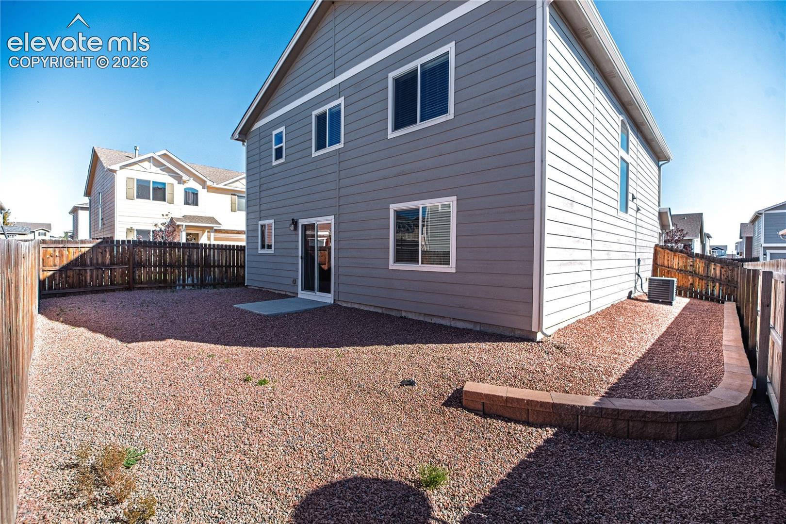 Gray horizontal siding with white trim, sliding glass door, and a low retaining wall
