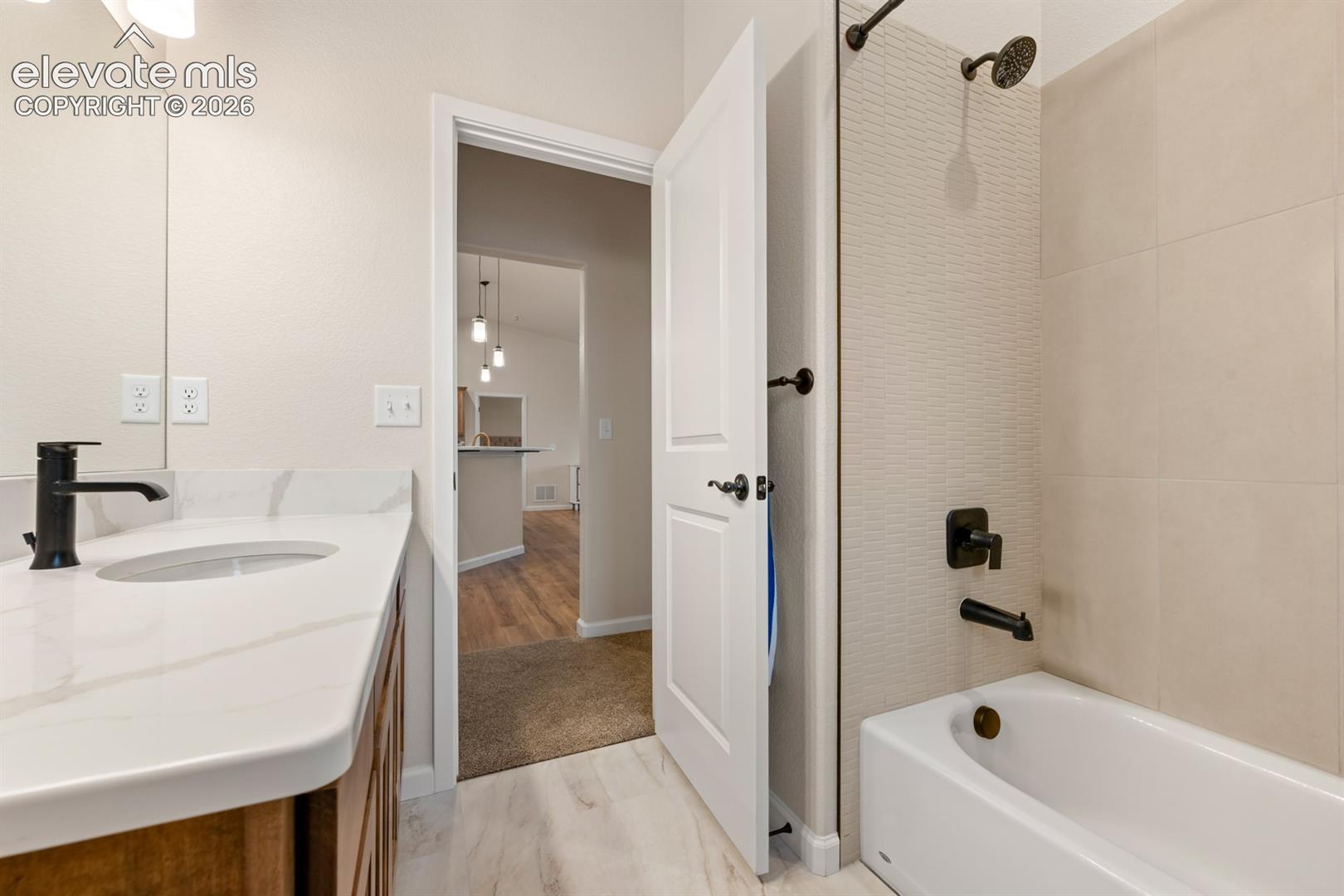 Bathroom featuring a vanity with a stone-finish countertop, matte black fixtures, an integrated tub-shower combination with textured tile surround, and wood-finish flooring