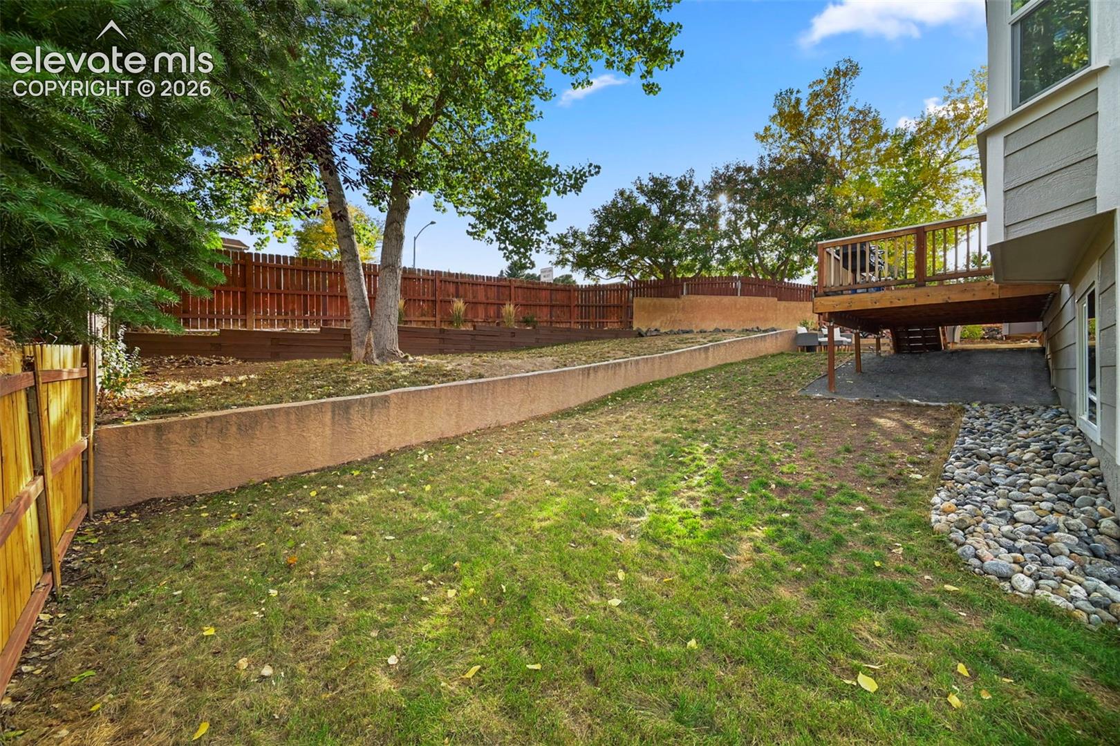 Expansive backyard featuring a multi-level wood fence, mature trees, a retaining wall, and a wood deck