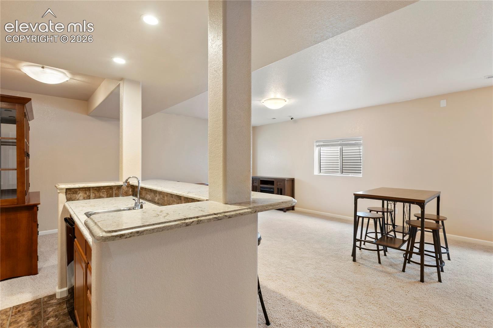 Built-in wet bar with a single basin sink, light-toned countertop, and tiled backsplash