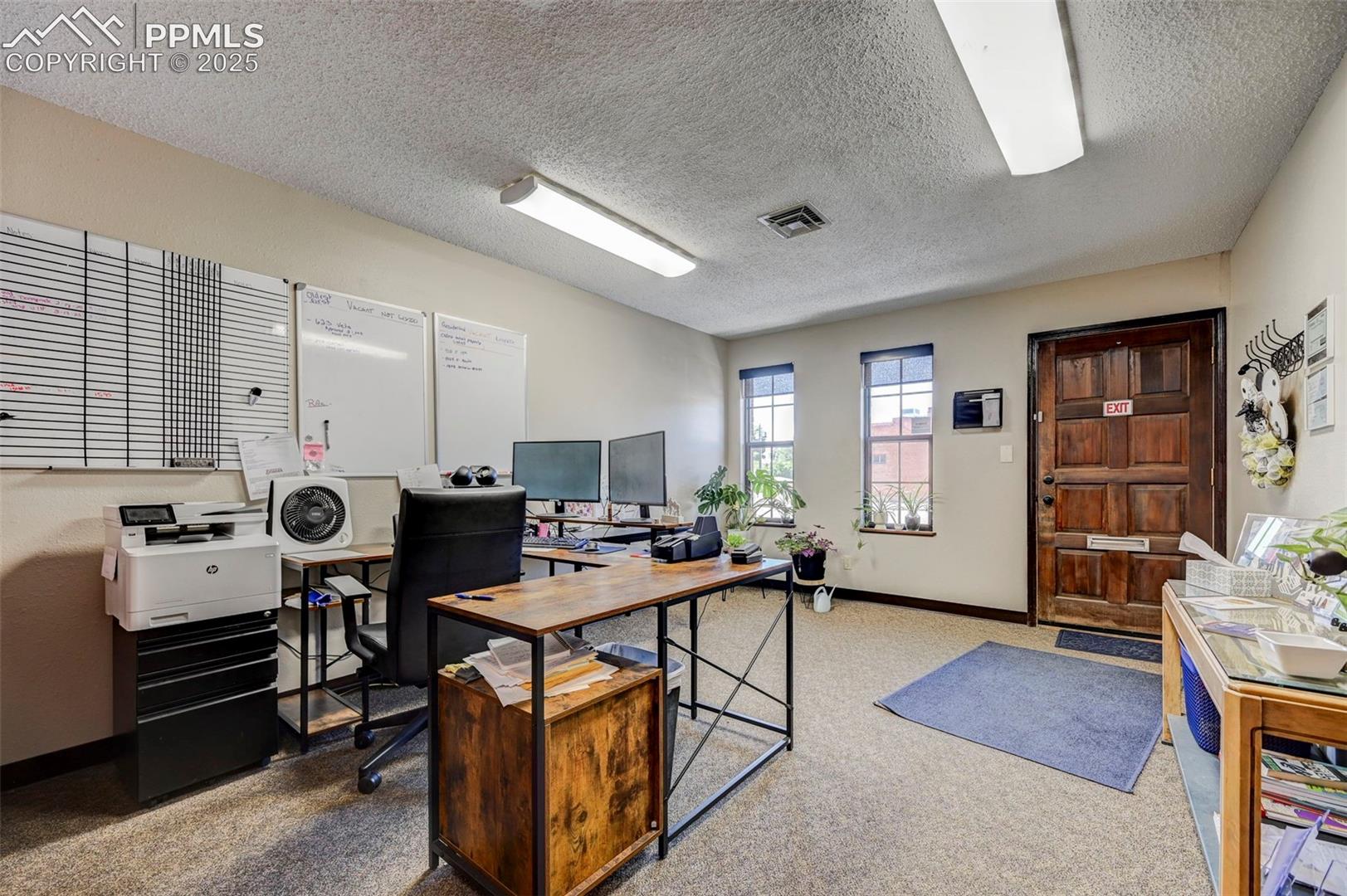 Office space with a textured ceiling, carpet flooring, and baseboards