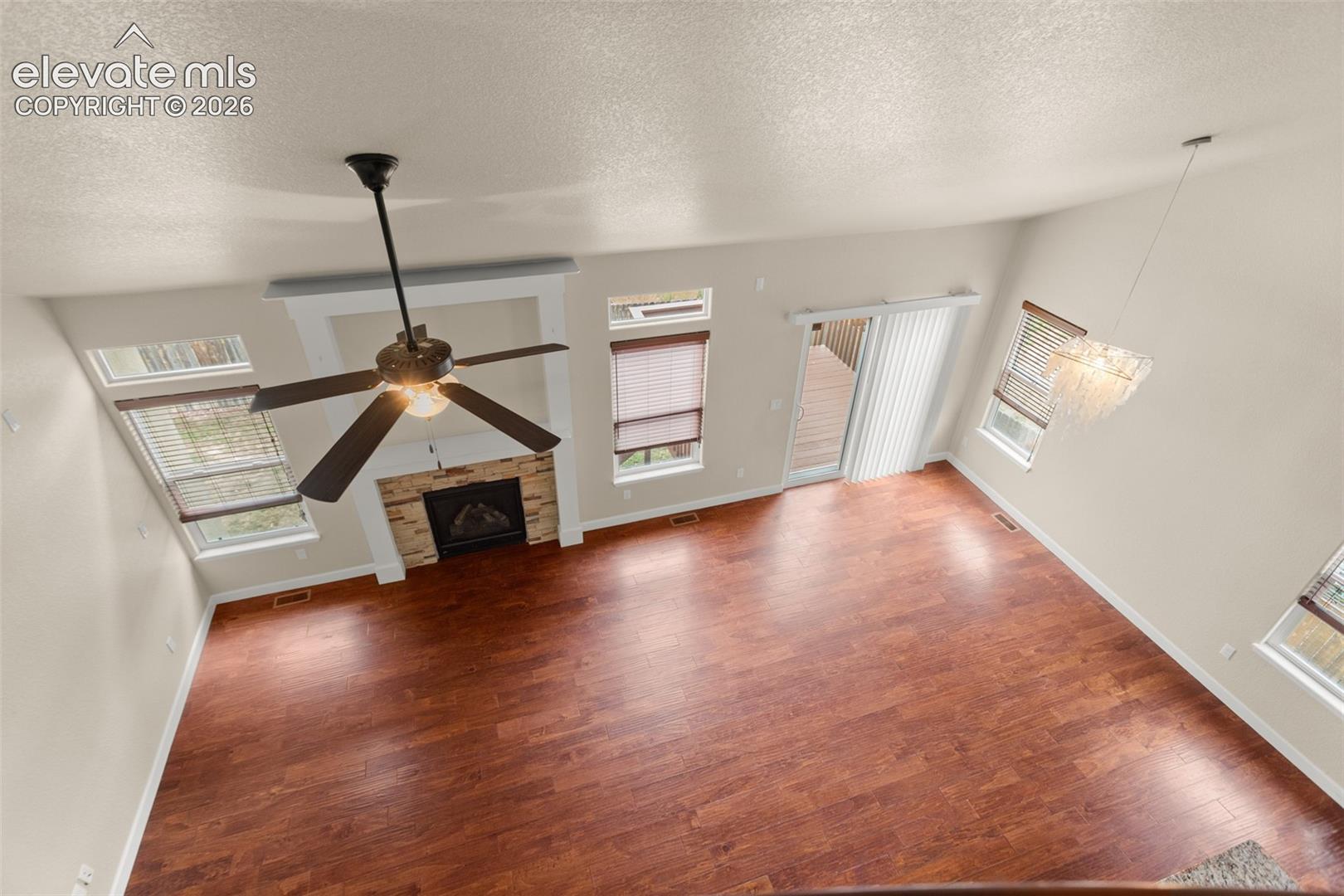 Vaulted ceilings featuring a central ceiling fan, wood-finish flooring, stone-surround fireplace, and multiple windows