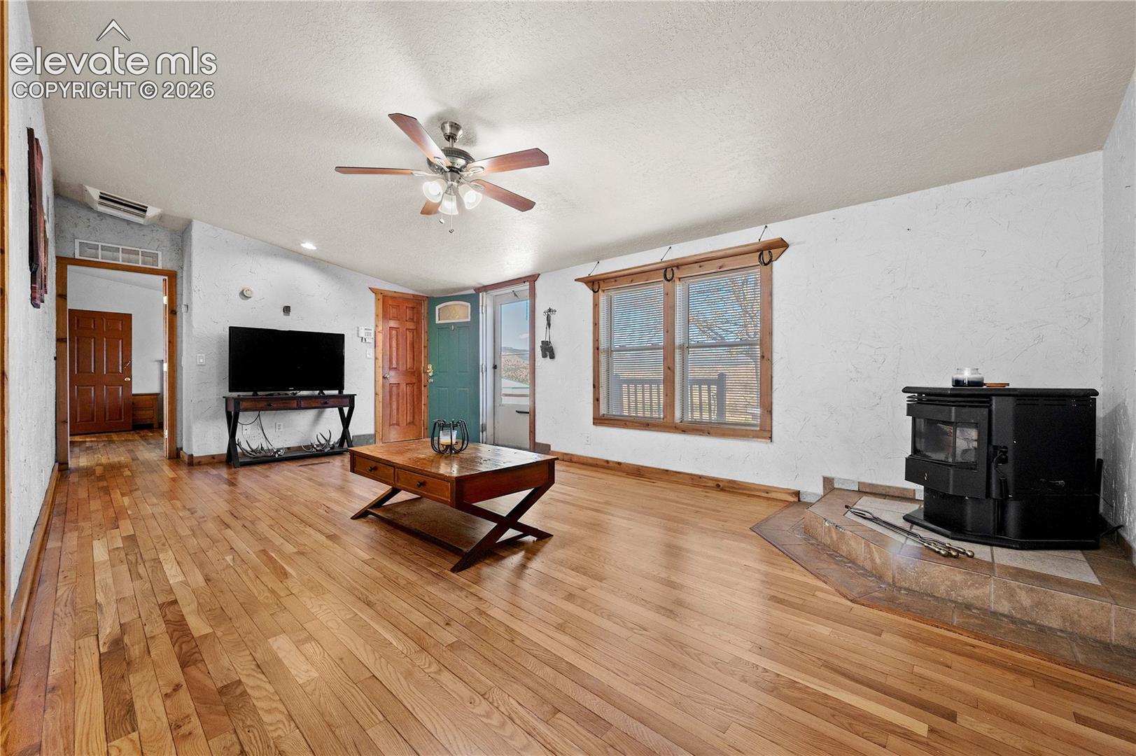 Living room with light hardwood / wood-style flooring, a textured ceiling, a wood stove, and ceiling fan